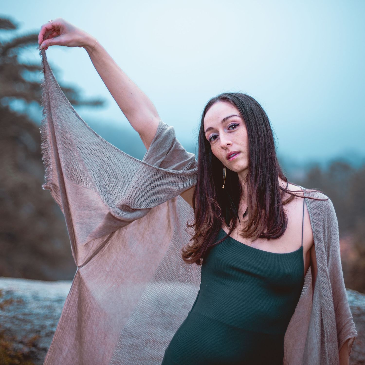 Dancer-like pose with flowing fabric against moody blue backdrop.