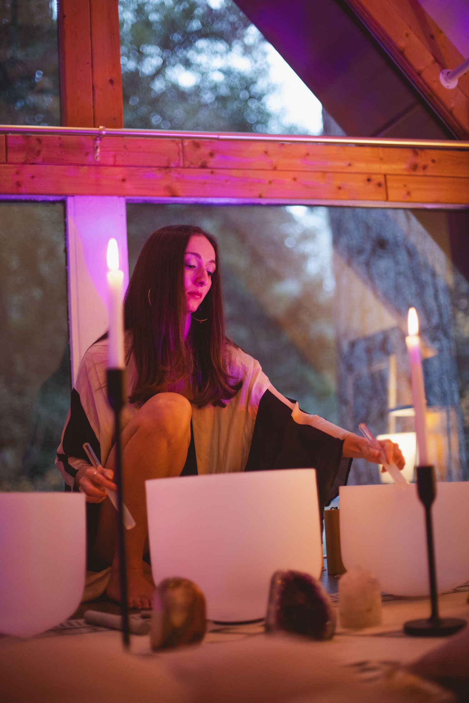 Indoor ceremony setup with white bowls and candles under wooden beams with purple lighting.
