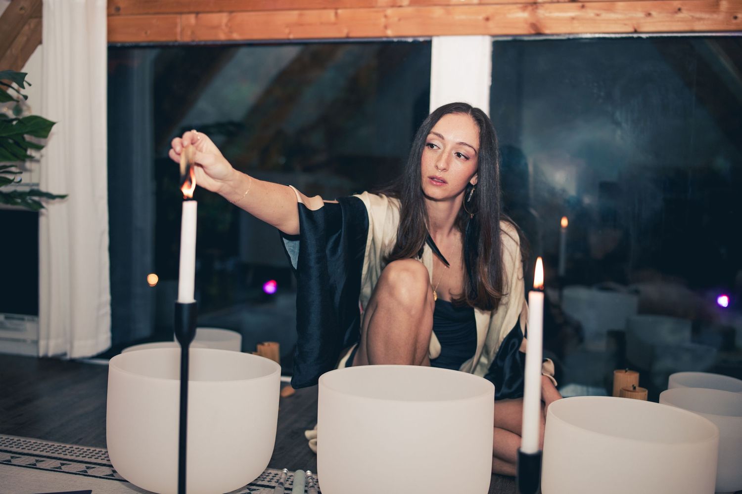 Woman in elegant dress lighting candles at an evening event setup.