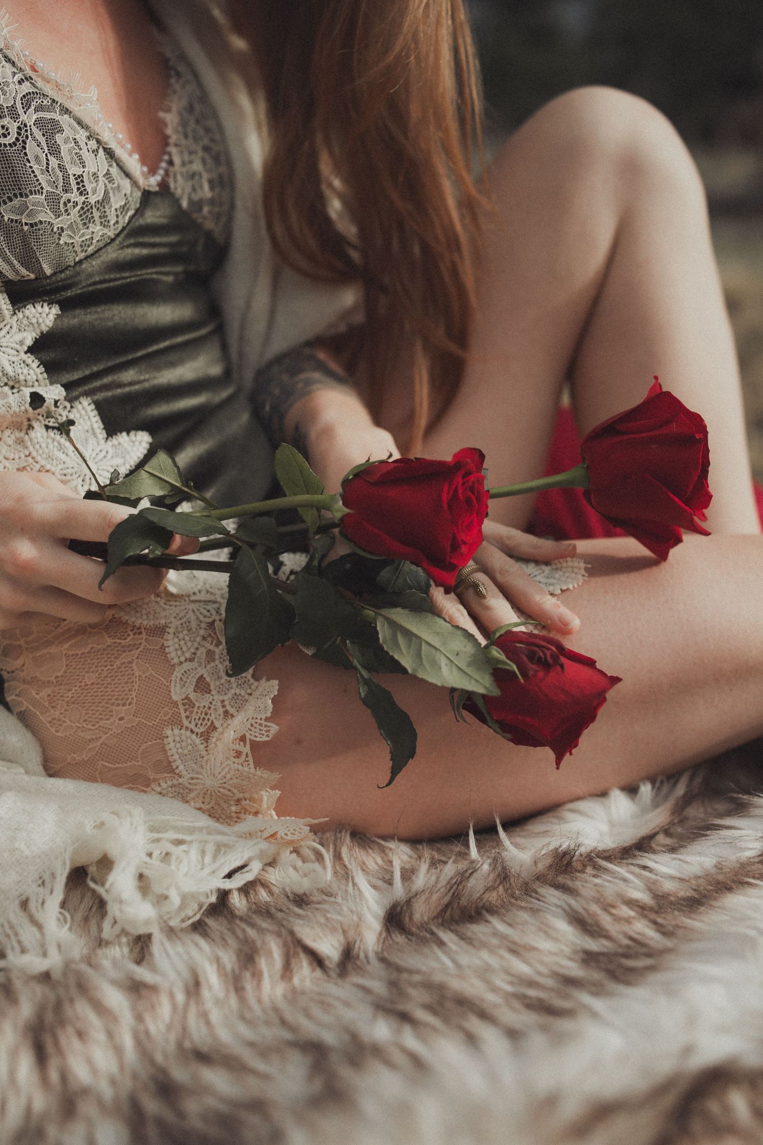 A person in lace holding vibrant red roses while resting on a plush fur blanket.