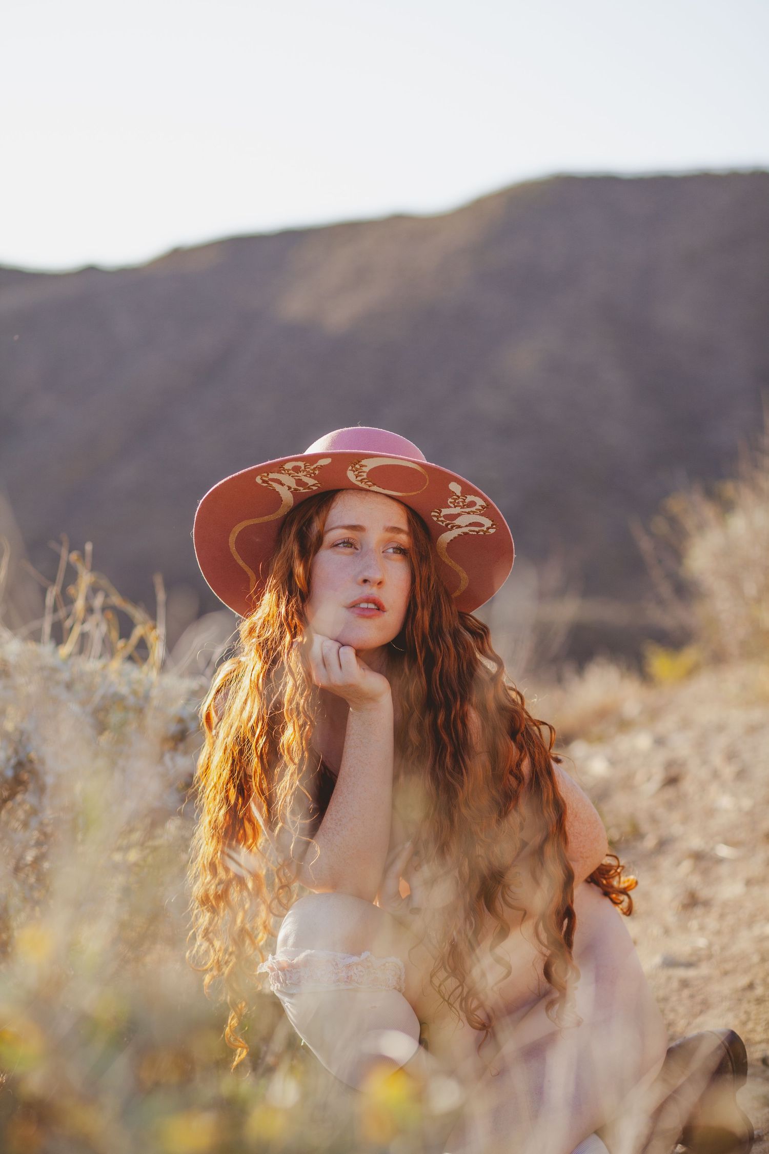 Dreamy outdoor portrait with wide brim hat in golden desert landscape at sunset.