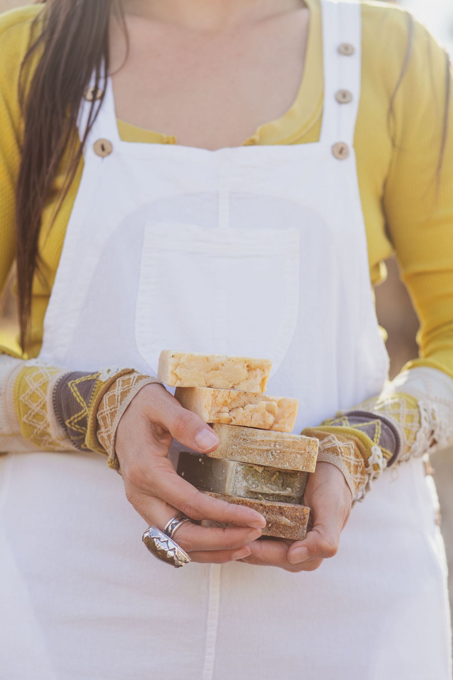 Hands holding handmade soap bars while wearing a white apron and yellow cardigan.