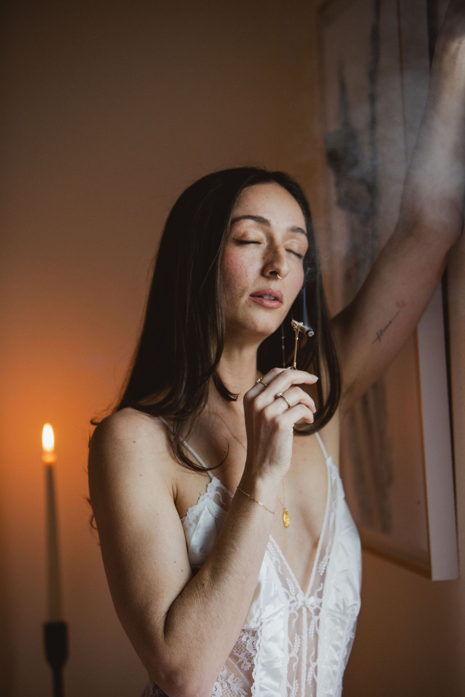 A sequence of moody candlelit portraits showing a woman in white lingerie taking a drag from a cigarette.
