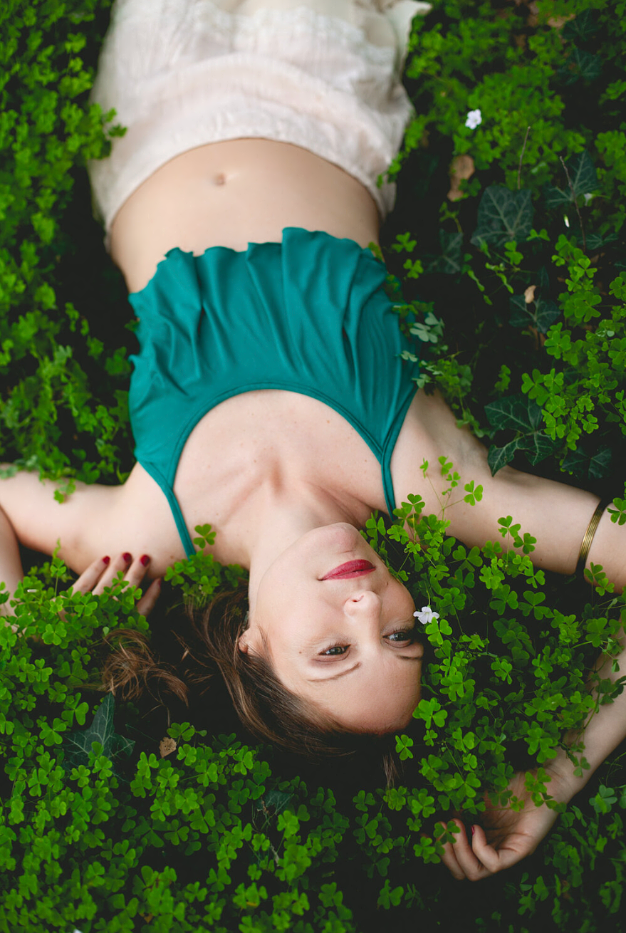 Ethereal portrait of someone lying in a bed of clovers wearing teal and white.