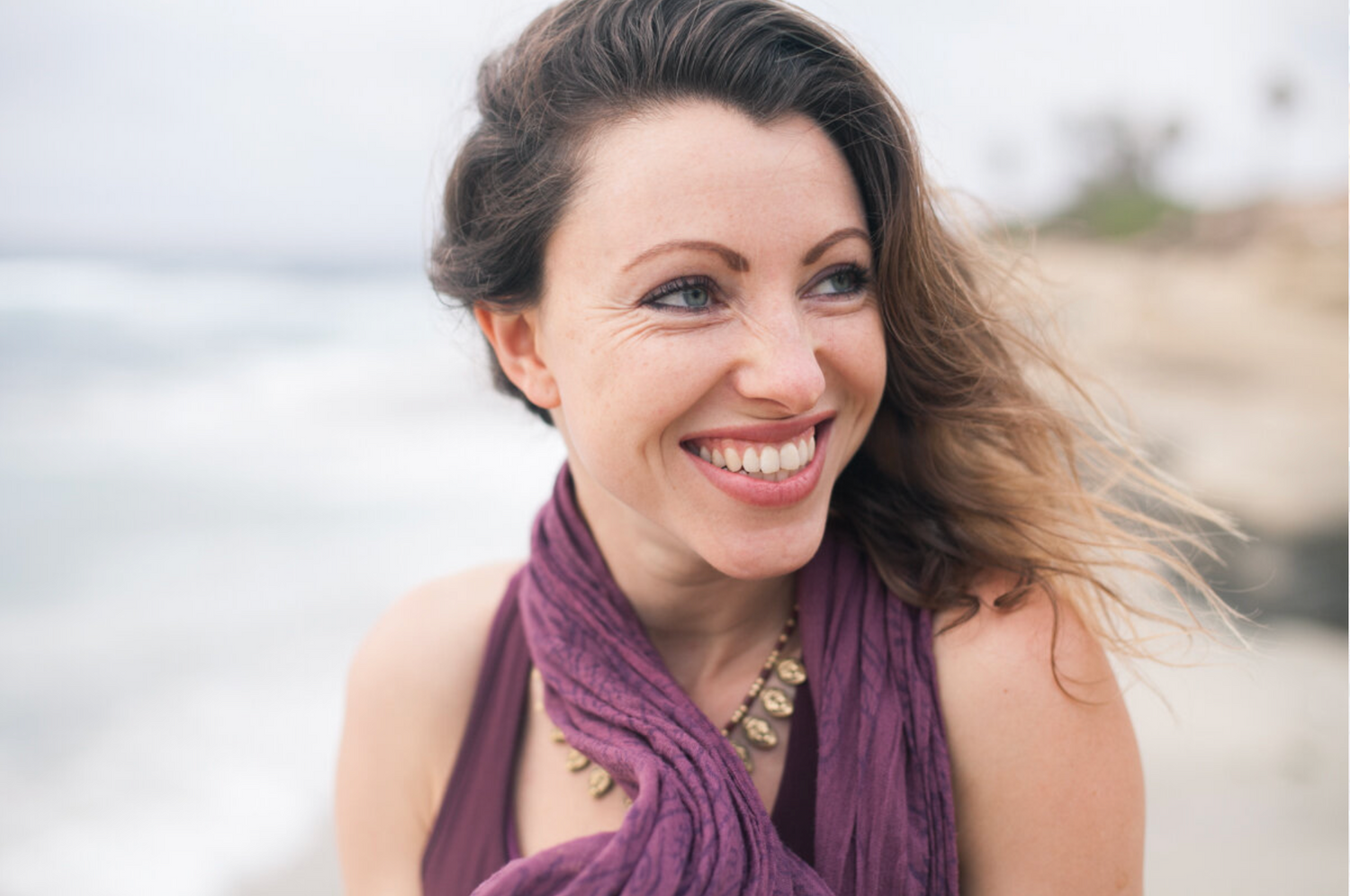 Seaside portrait wearing purple scarf with wind-swept hair.