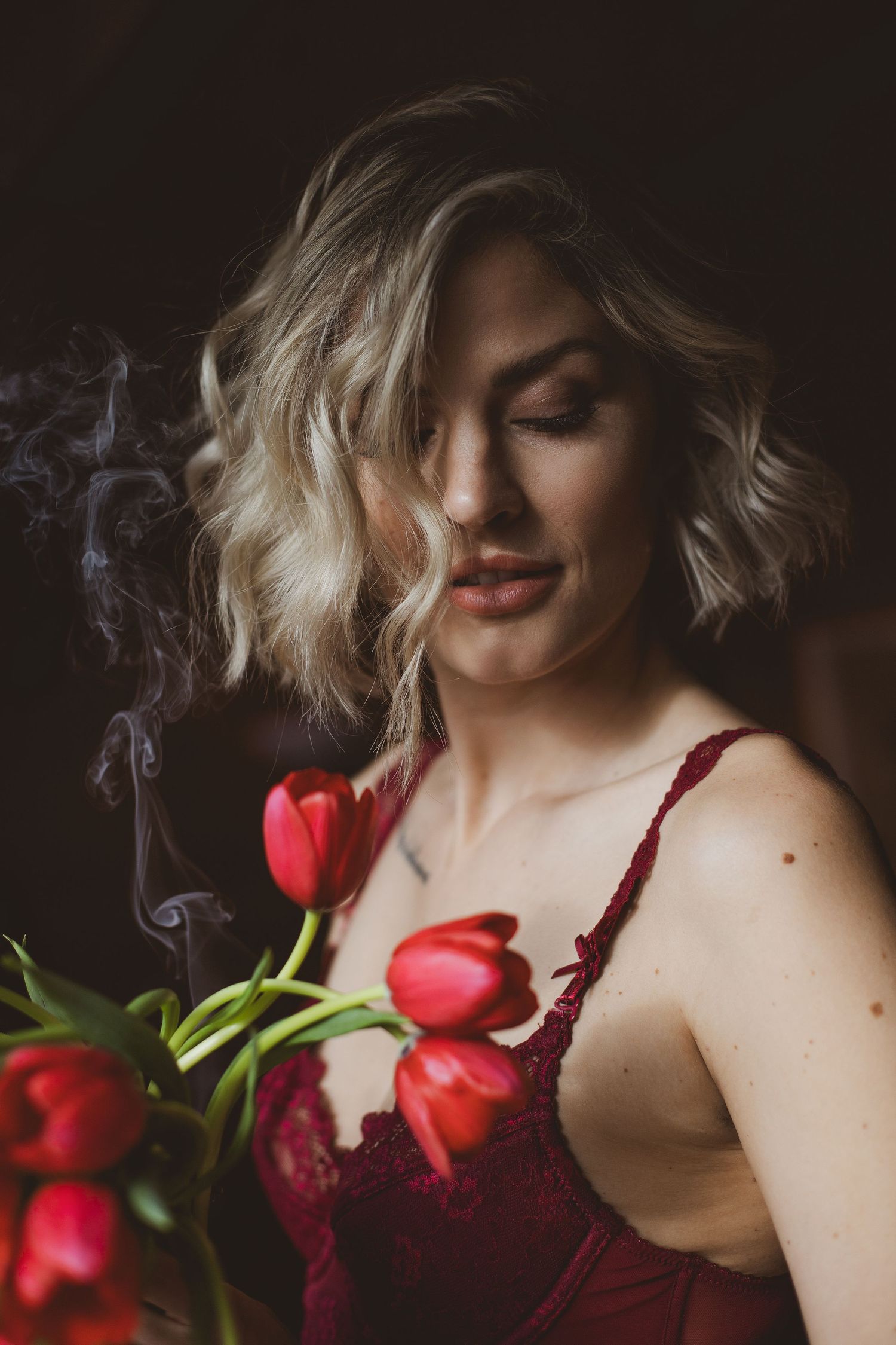 Moody portrait with red tulips and wisps of smoke against dark background.
