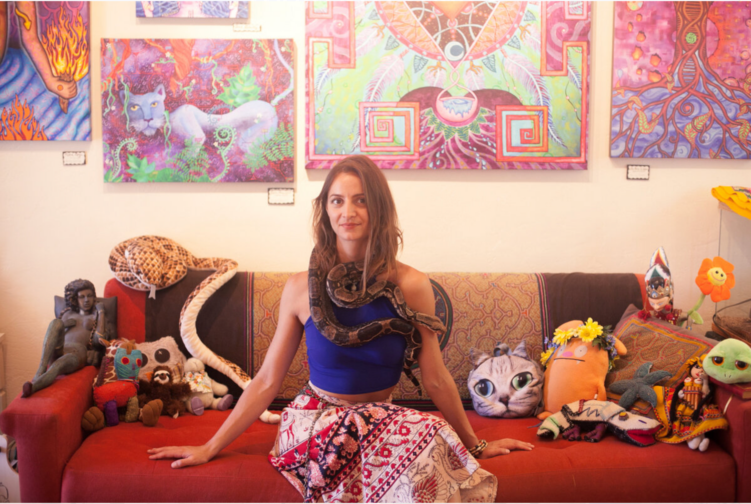 Colorful art hangs on walls above a couch decorated with plush toys and decorative pillows.