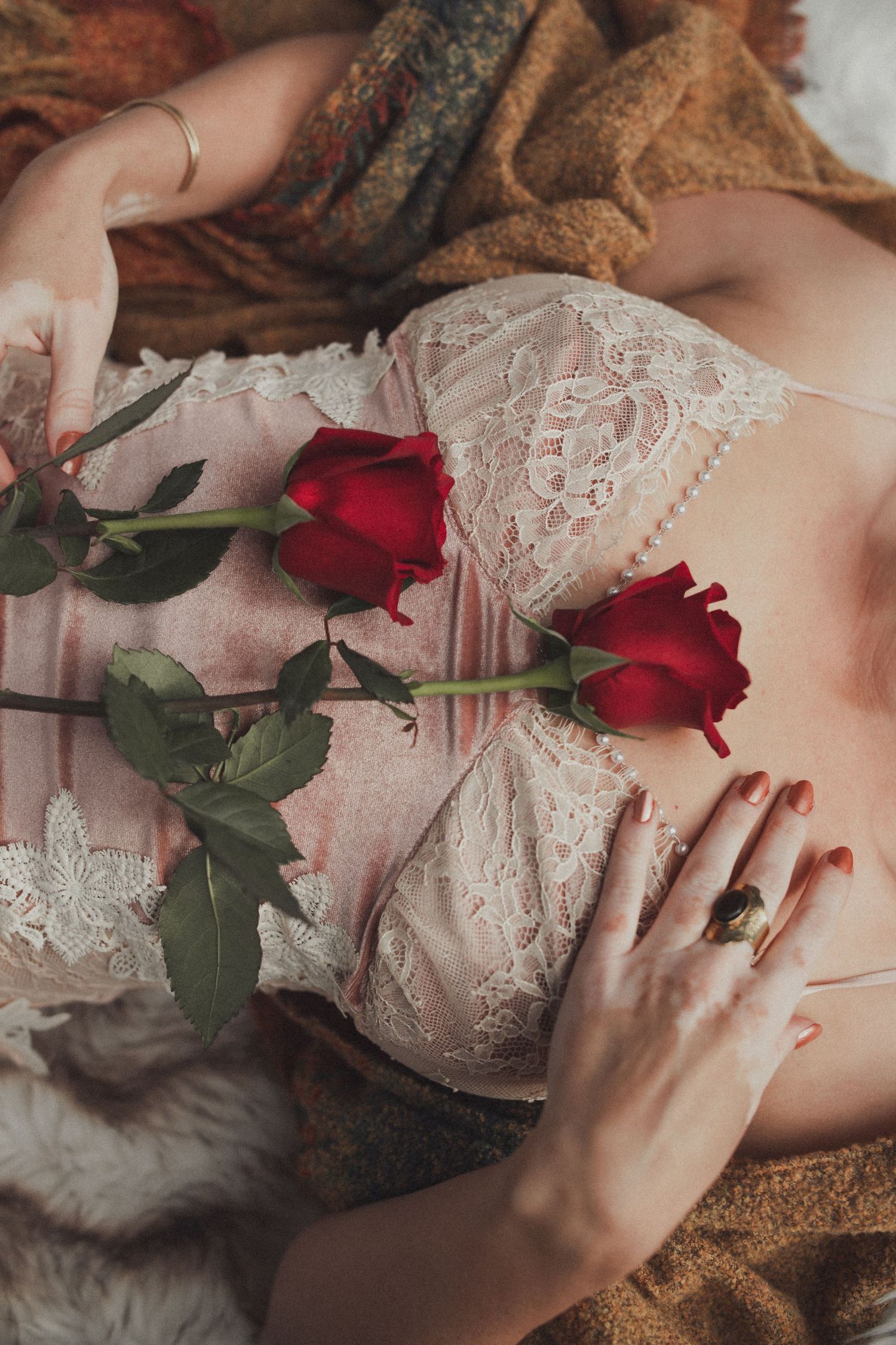 Romantic composition with red roses against delicate white lace lingerie and soft fabric textures.