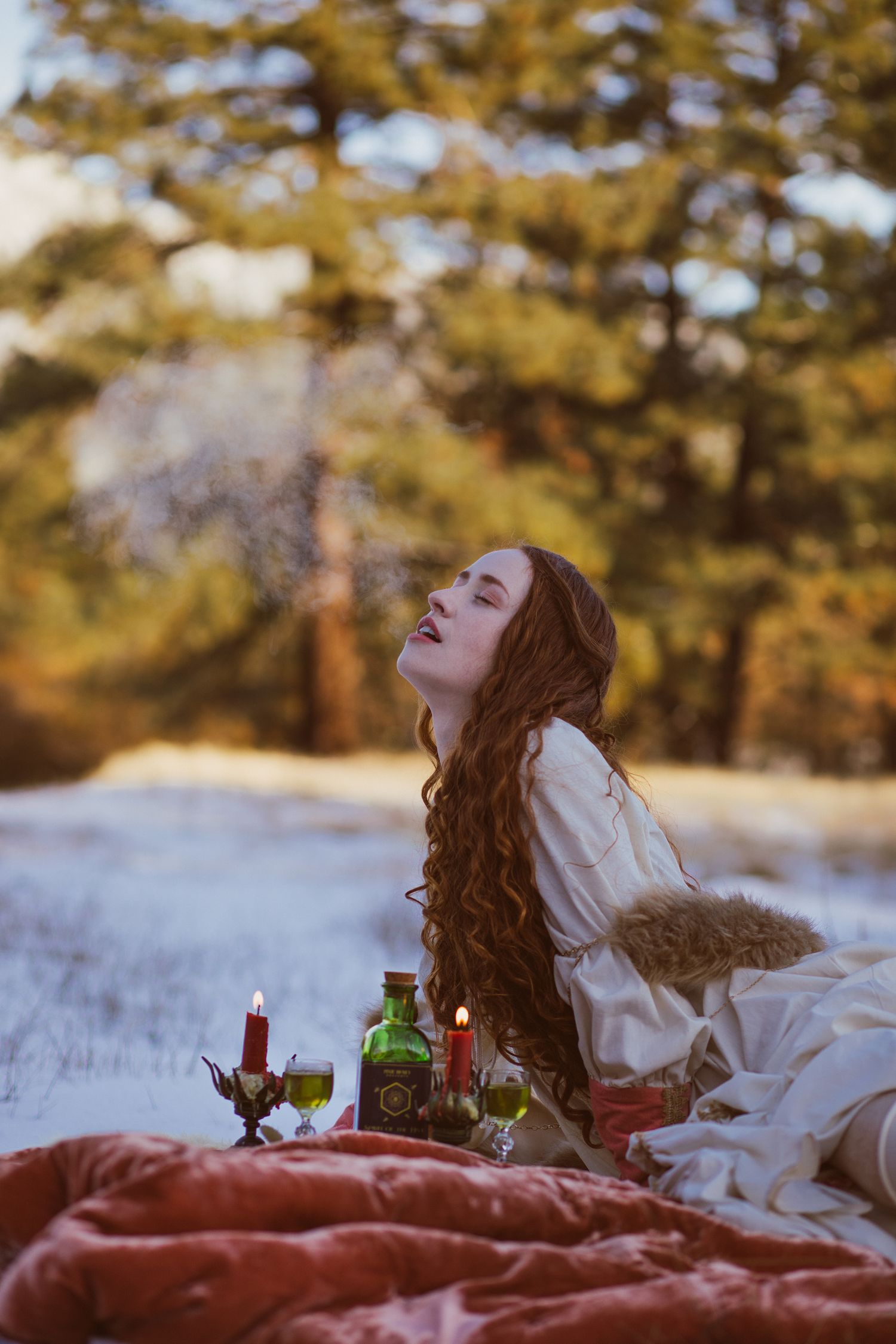 Romantic winter picnic scene with wine and candles on snowy ground.