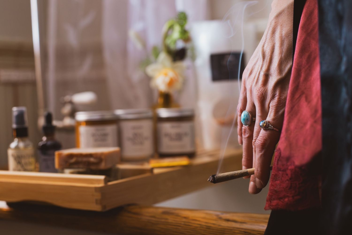Hand holding a dropper bottle over a wooden tray with various aromatherapy supplies.