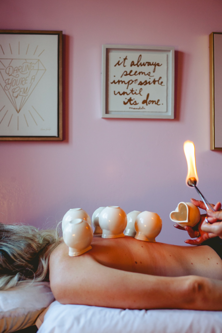 Cupping therapy setup with burning flame and healing crystals against pink wall with inspirational artwork.