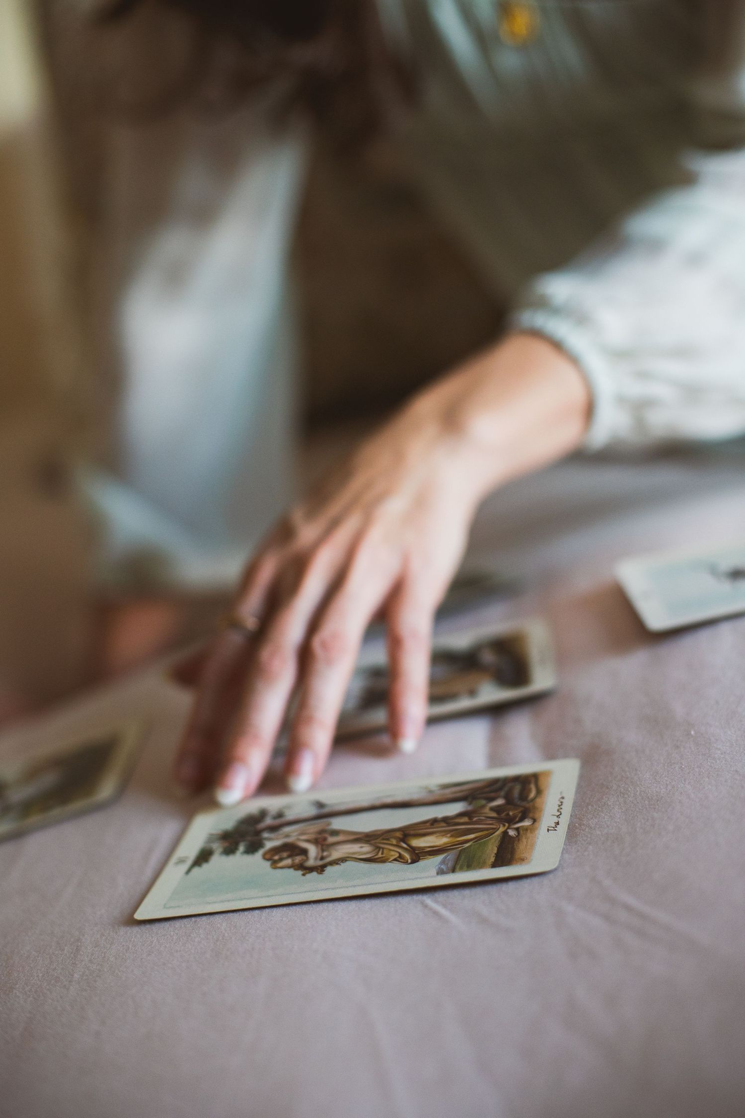 A hand reaches out to touch vintage photographs laid out on a soft fabric surface in muted lighting.