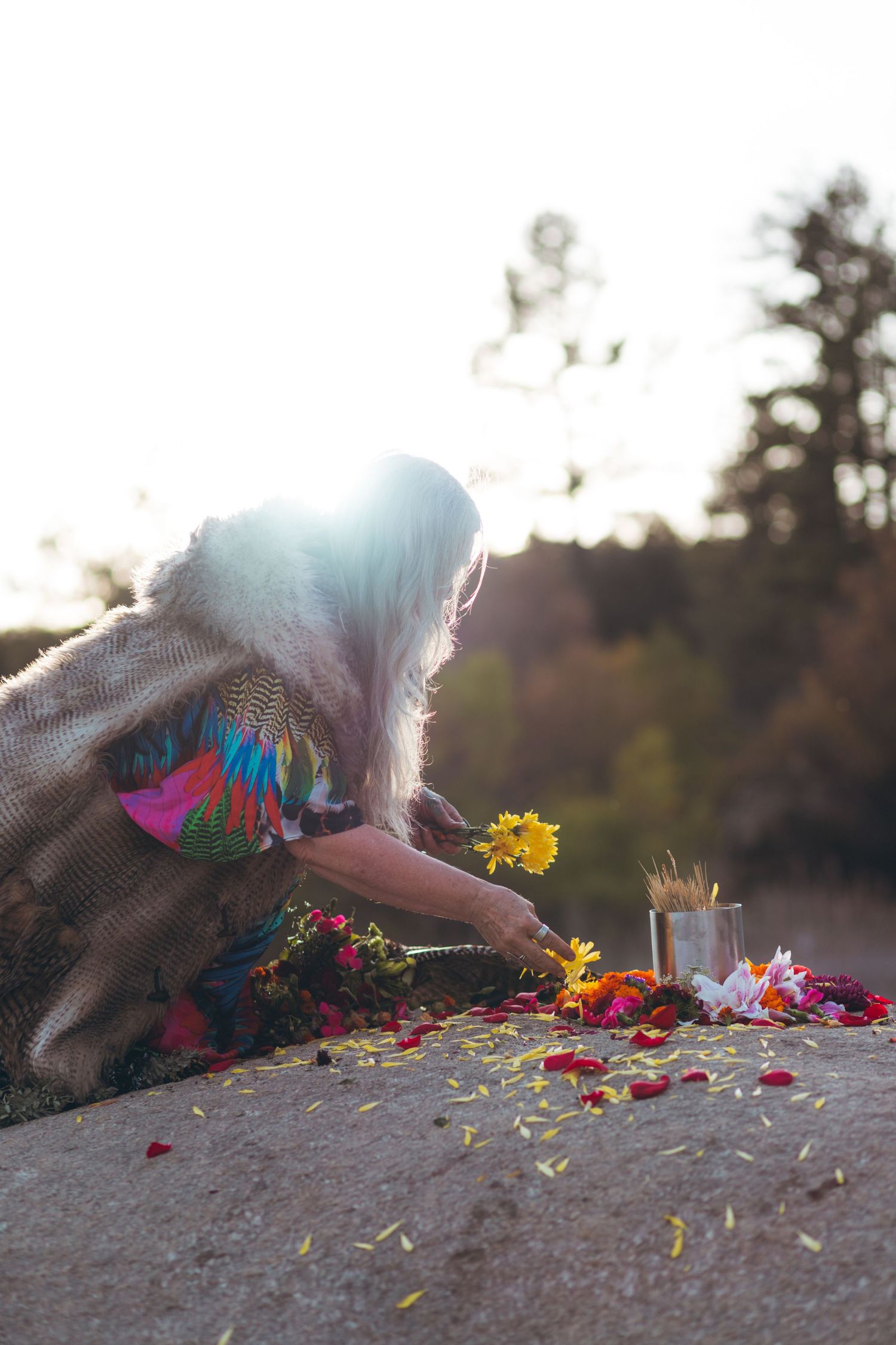Person in flowing garments arranges flowers and candles during sunset ceremony.