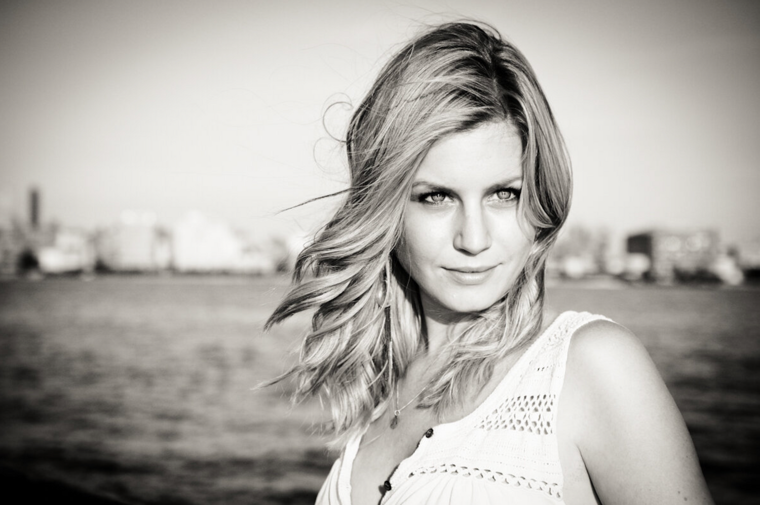 Black and white portrait with soft lighting against urban waterfront backdrop.
