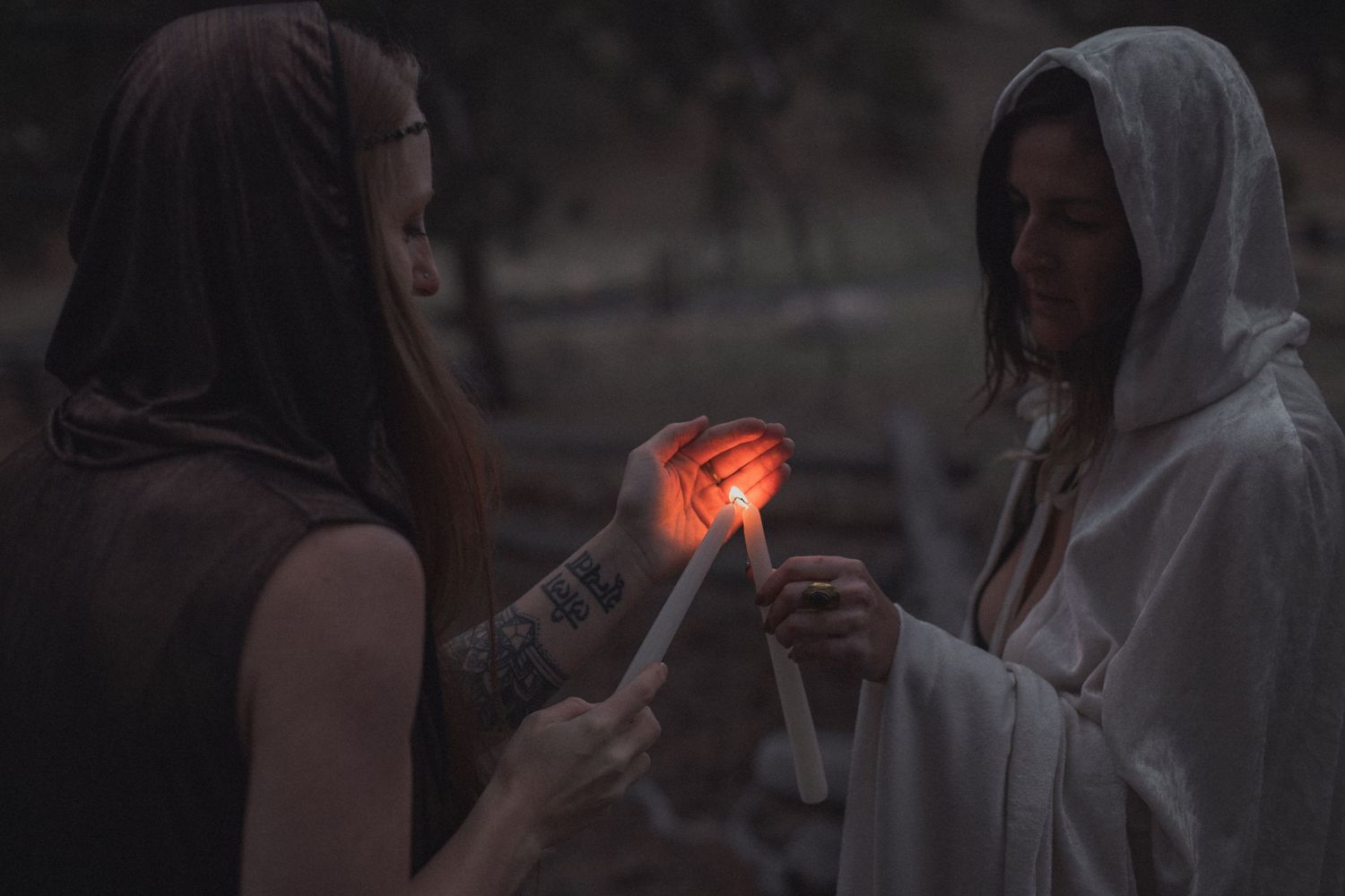 Two figures in hooded cloaks stand close together holding a glowing red light in the darkness.