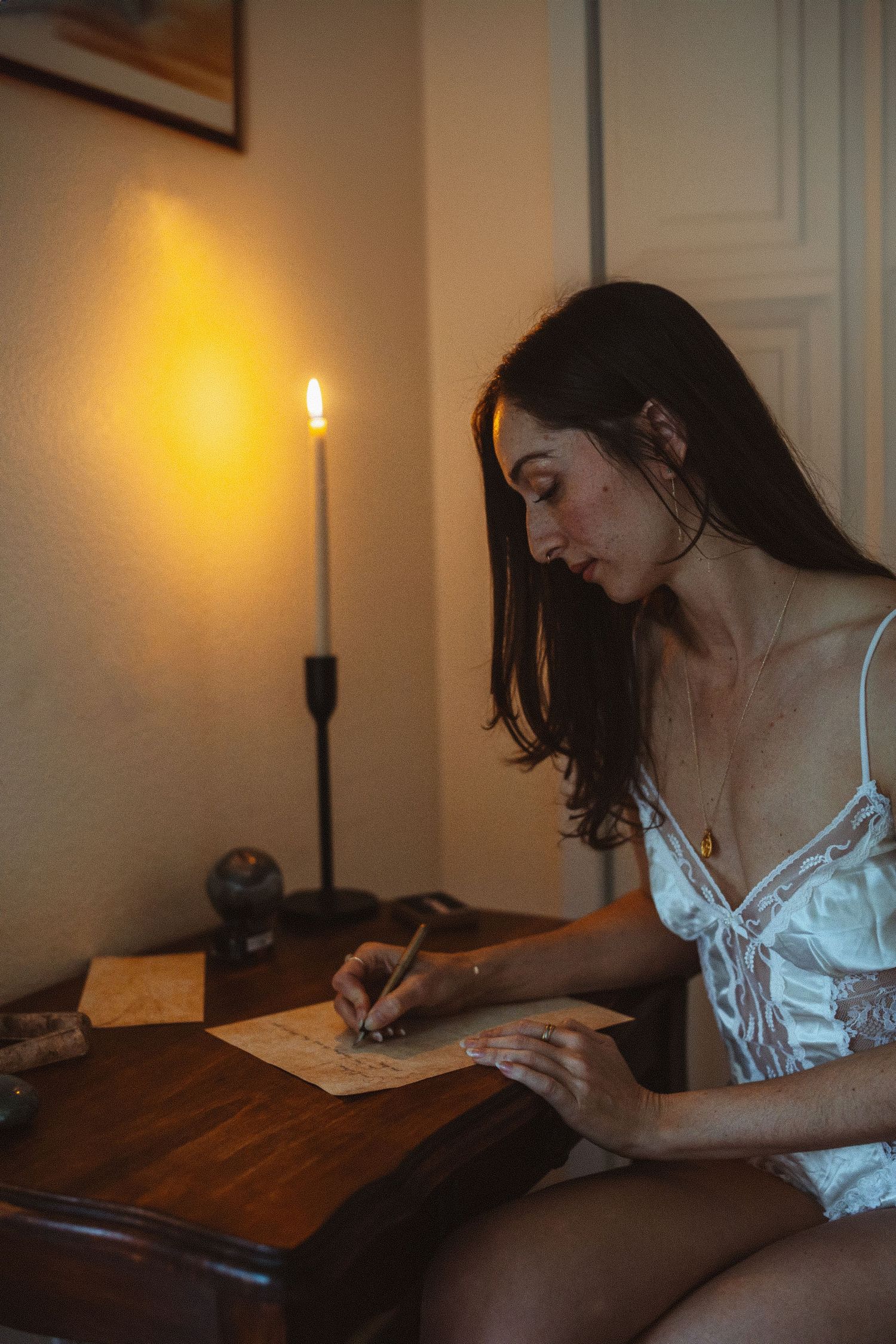 A person writes by candlelight at a wooden desk in a series of sequential photos showing different angles.
