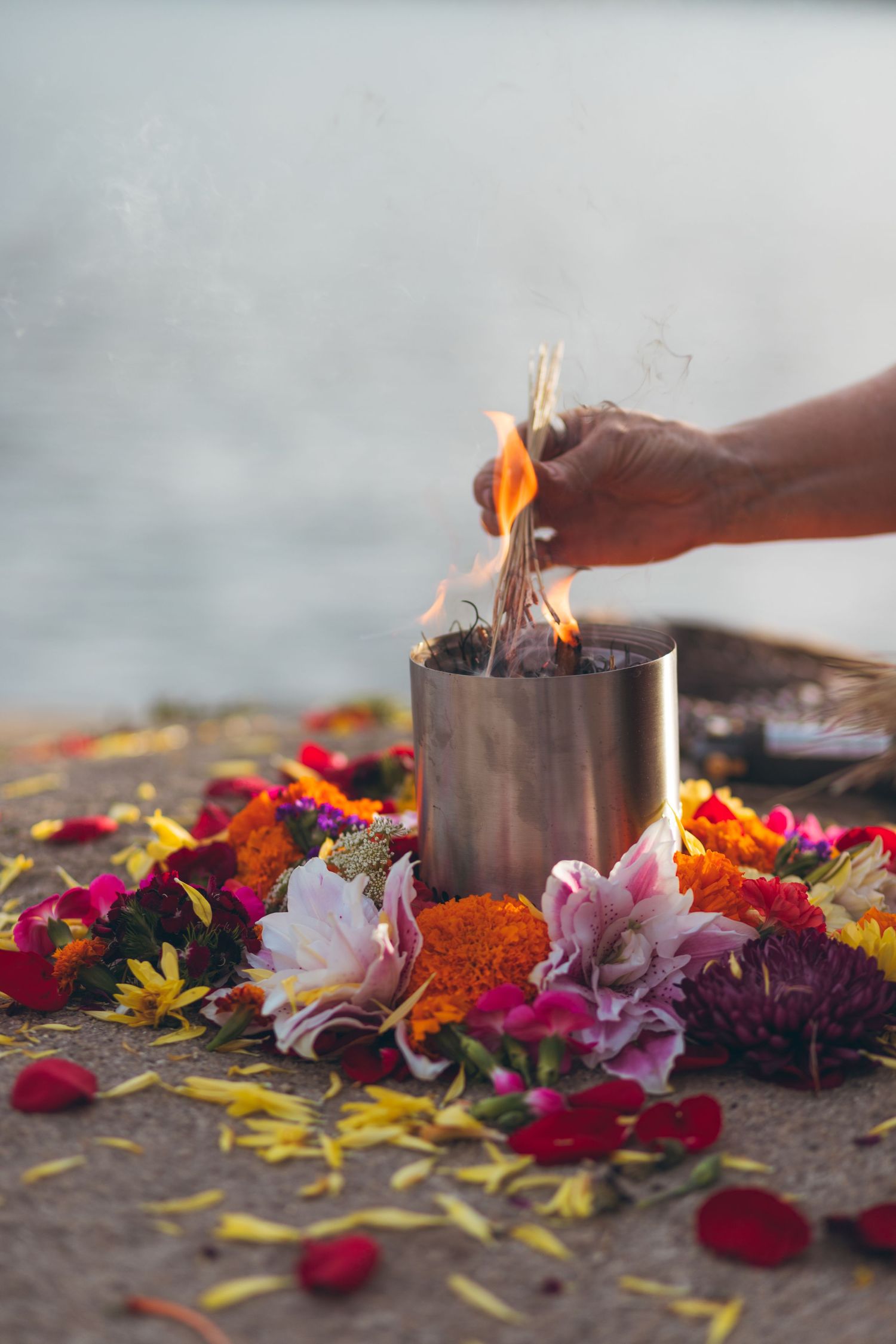 Hand lighting candles surrounded by colorful flower petals in a spiritual ceremony setting.