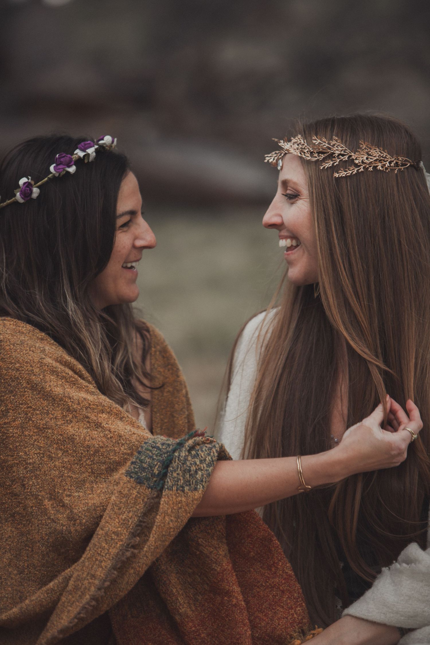 Two friends wearing floral crowns share a joyful moment together while wearing cozy autumn sweaters outdoors.