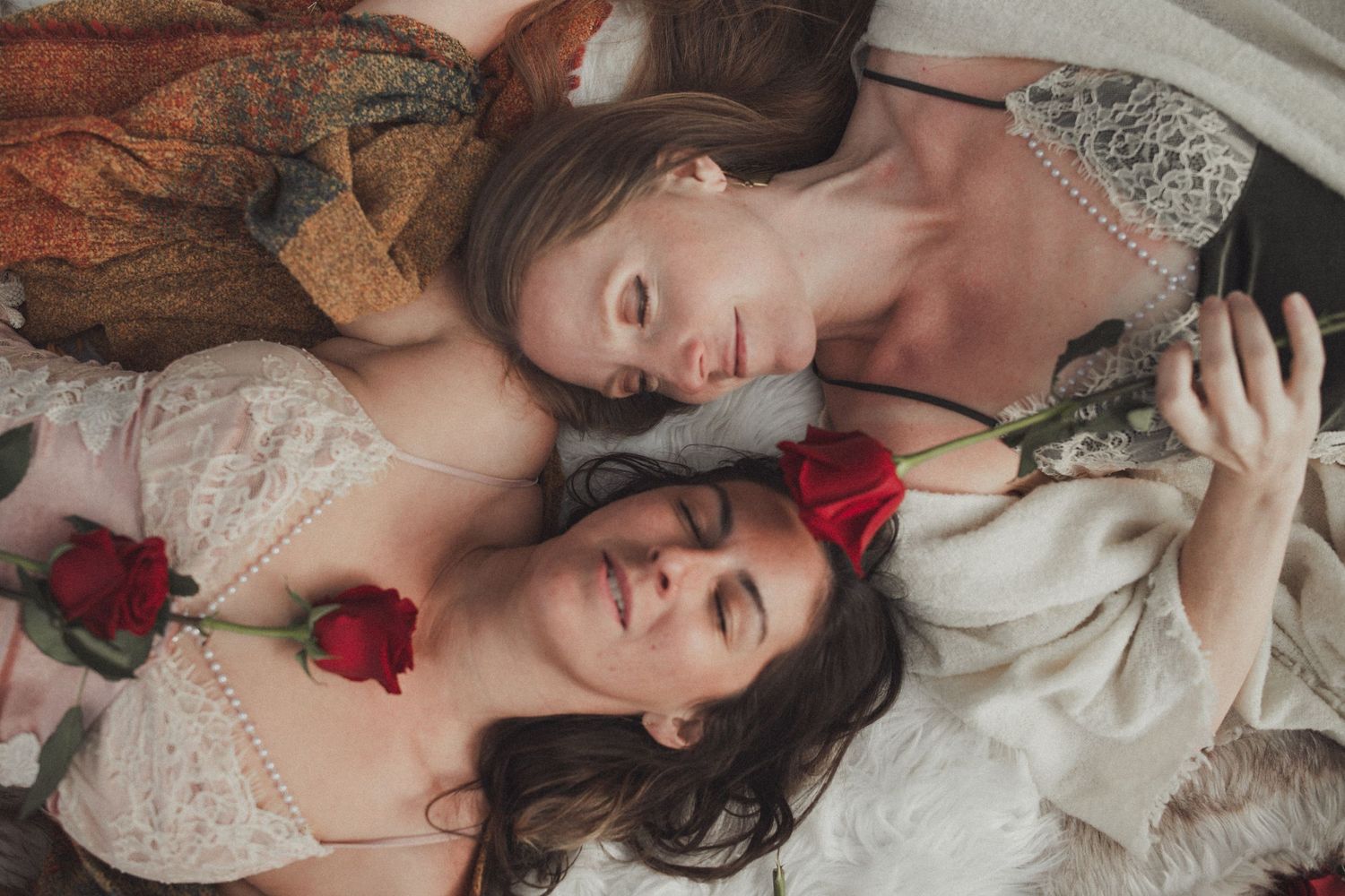 Two people lying down in white lace dresses with red roses and elegant vintage styling.