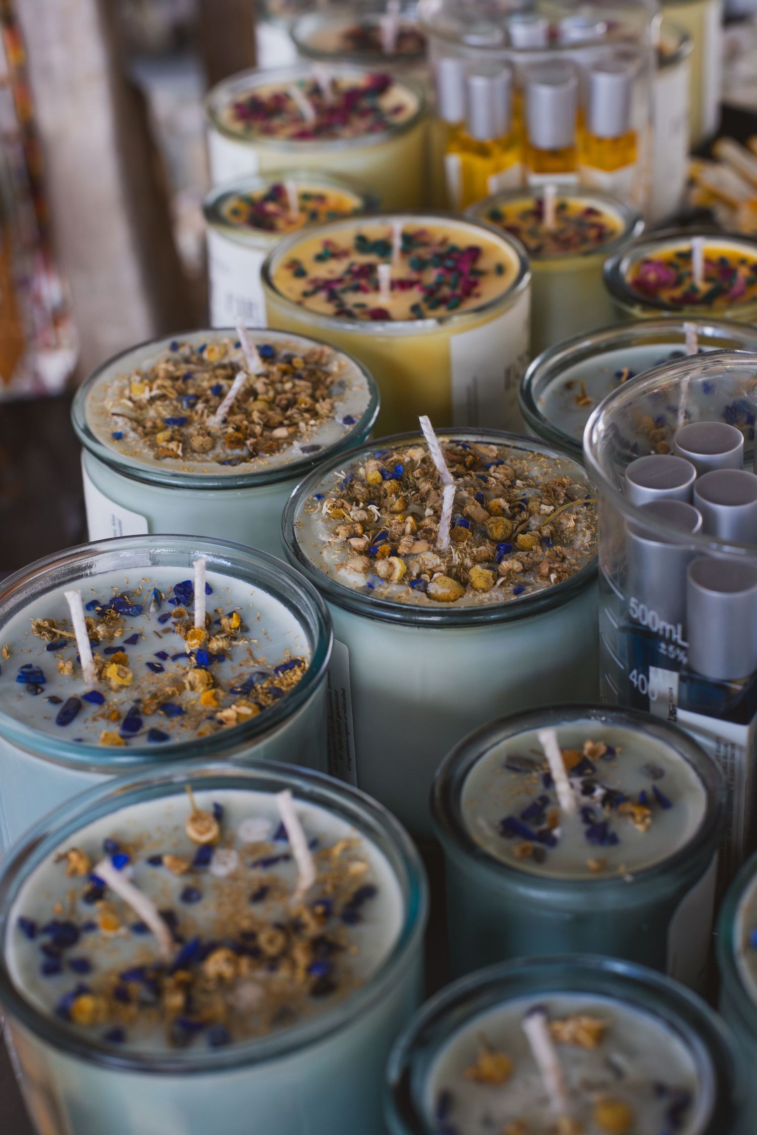 Handcrafted candles with dried flowers and herbs decorating their surfaces in glass jars.