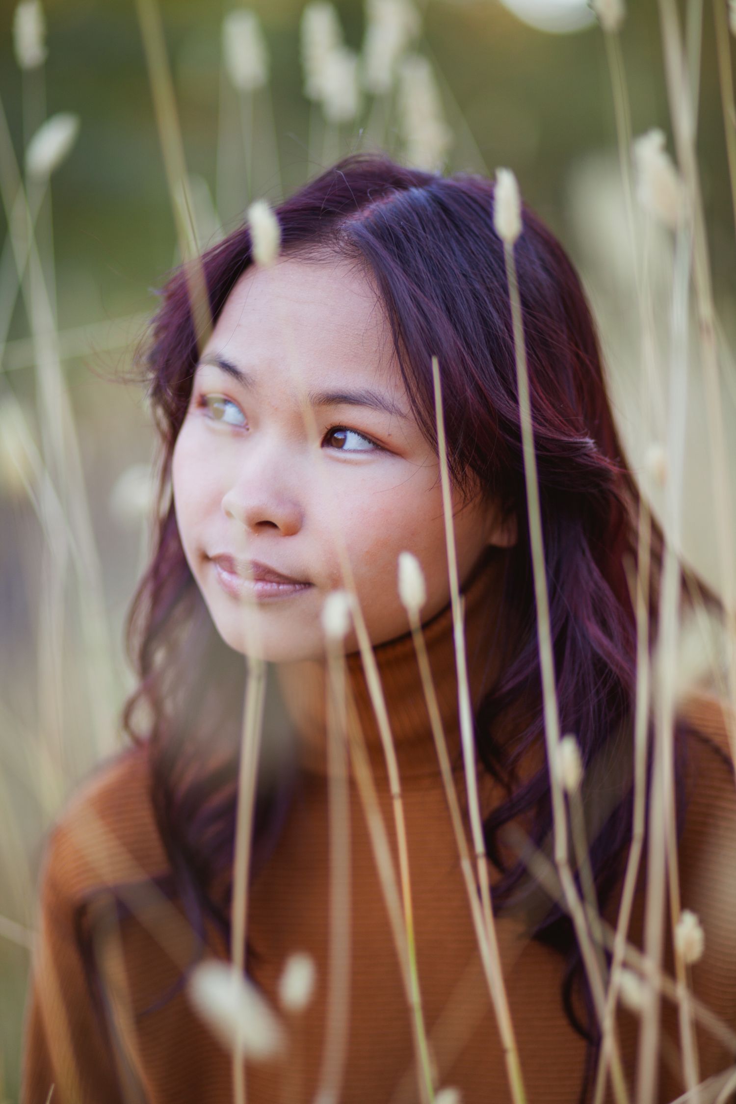 Ethereal portrait among tall grass with soft natural lighting and gentle expression.