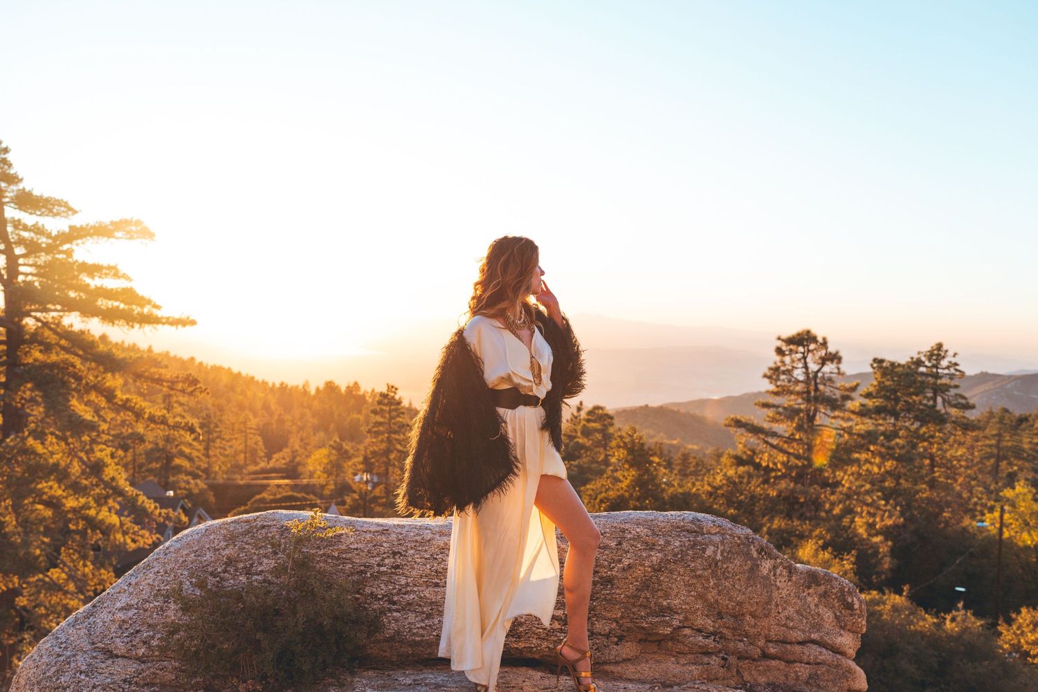 Silhouetted figure stands on rocky outcrop during golden hour sunset.