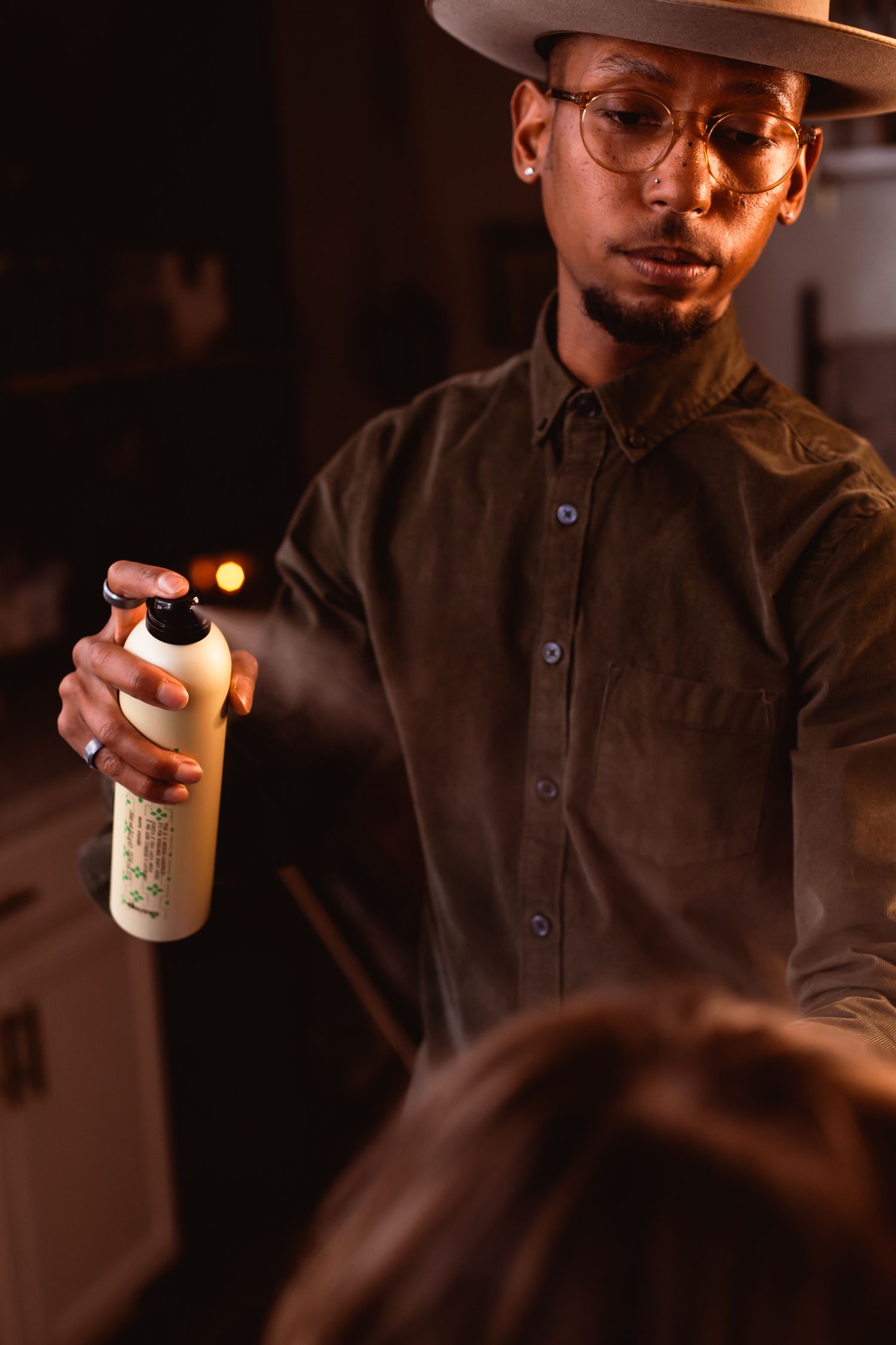 Person in dark attire and hat holding a product bottle in warm lighting.