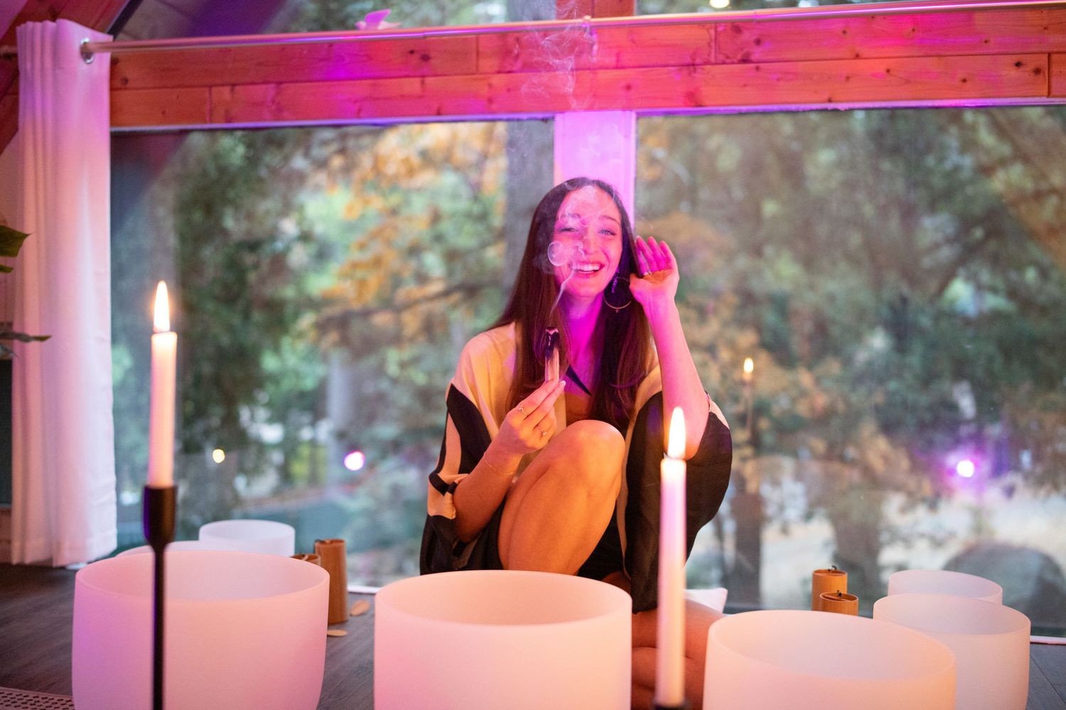 Person sitting among white candles under pink-lit pergola at dusk.