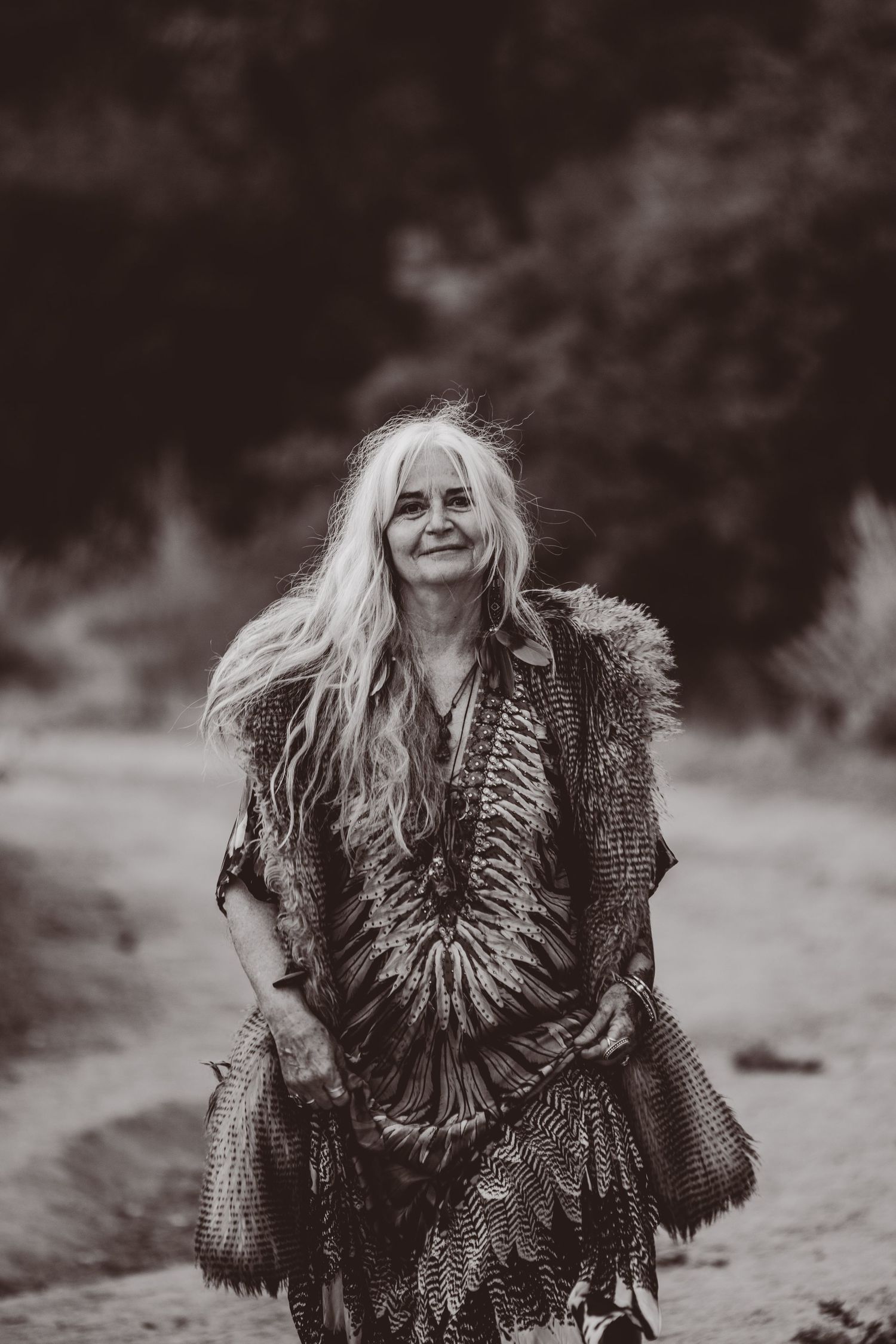 Black and white portrait of person in bohemian attire with flowing hair outdoors.