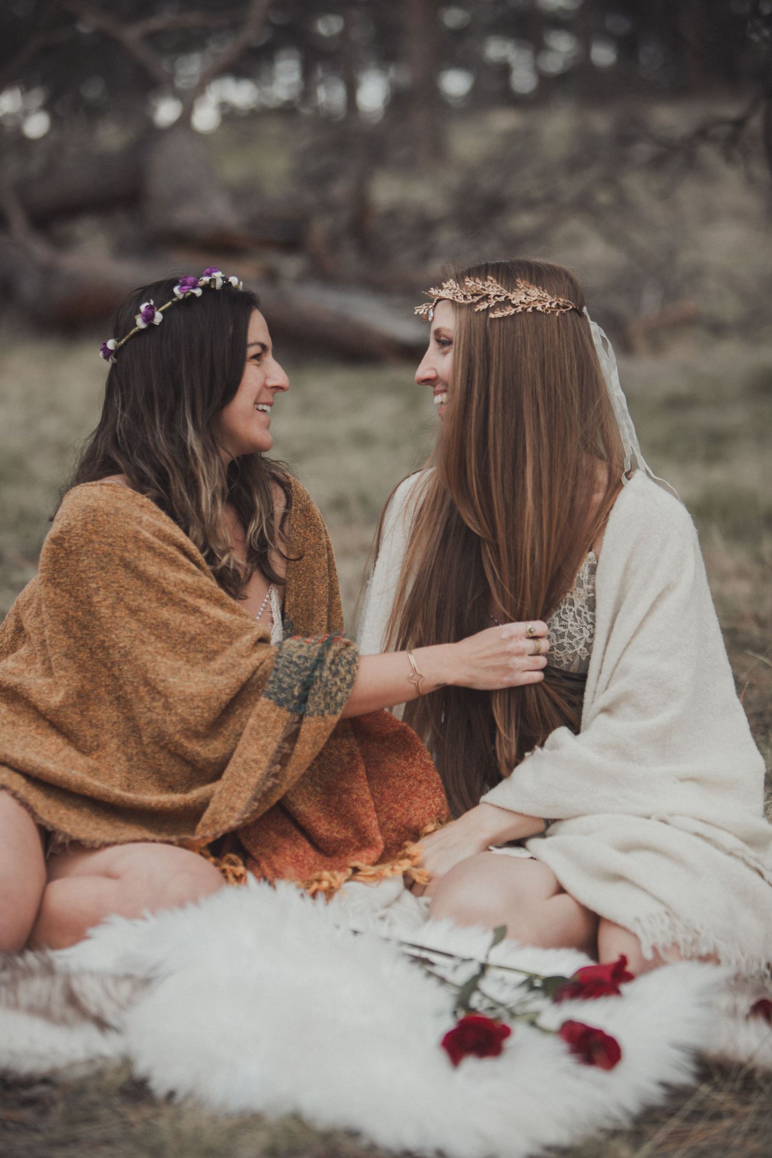 Two friends wearing floral crowns share a cozy moment on a blanket with roses in a dreamy outdoor setting.