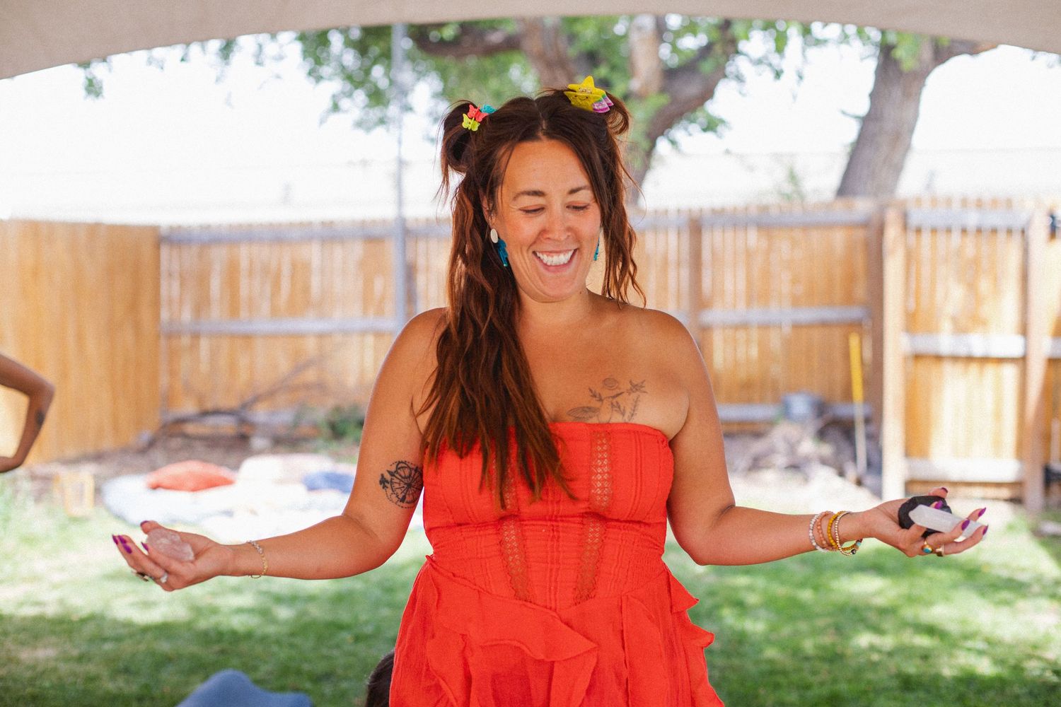 Woman in vibrant red dress with long dark hair dancing joyfully outdoors in backyard setting.