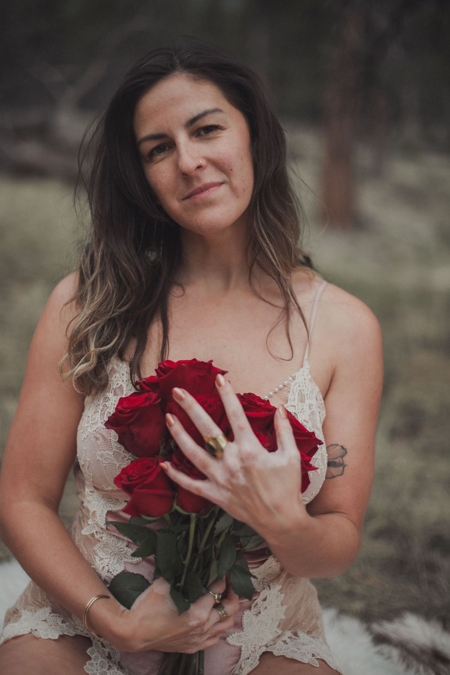 Someone in a lace dress holds a bouquet of vibrant red roses in a romantic outdoor portrait.