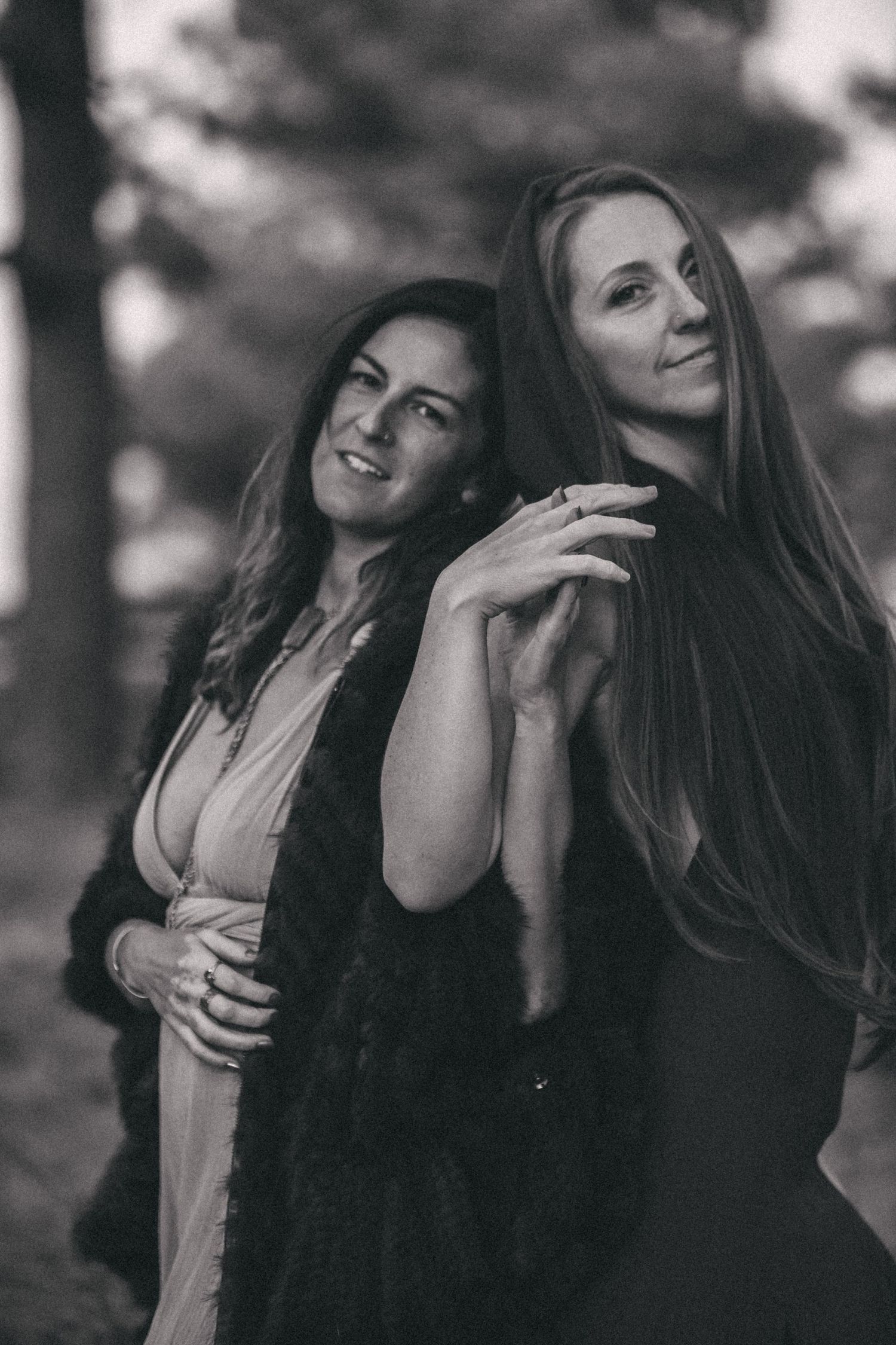 Two women in dark and light dresses pose together outdoors in a black and white artistic portrait.