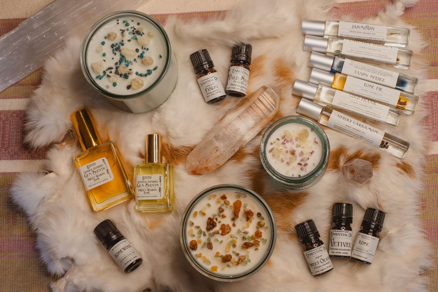 A flat lay of essential oils, perfume bottles, and decorative bowls with dried flowers on a textured fabric background.
