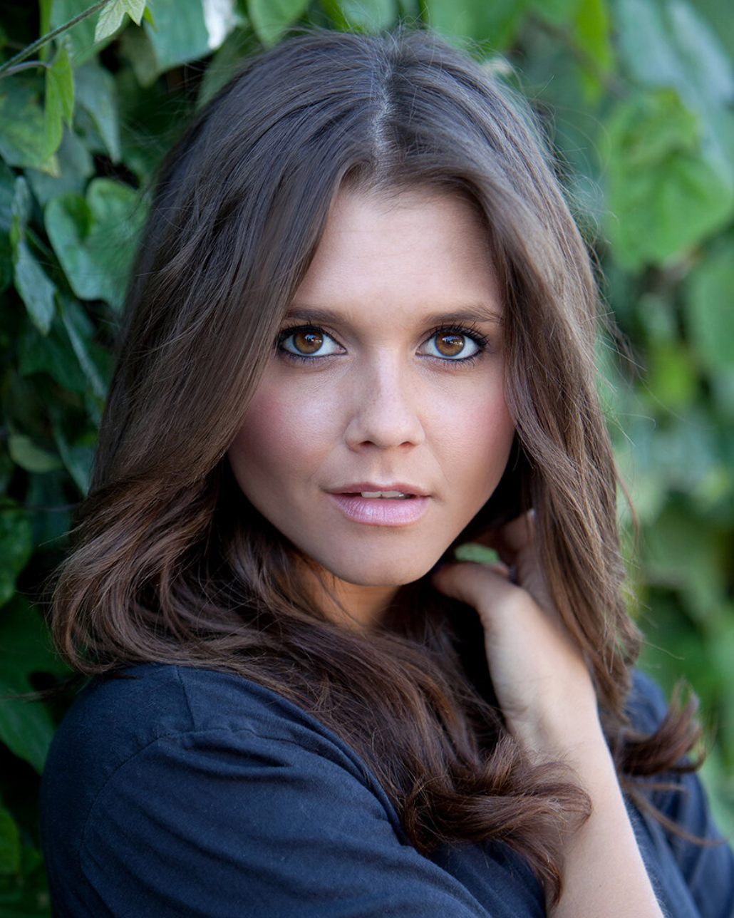 Portrait with long brown hair against green foliage background.
