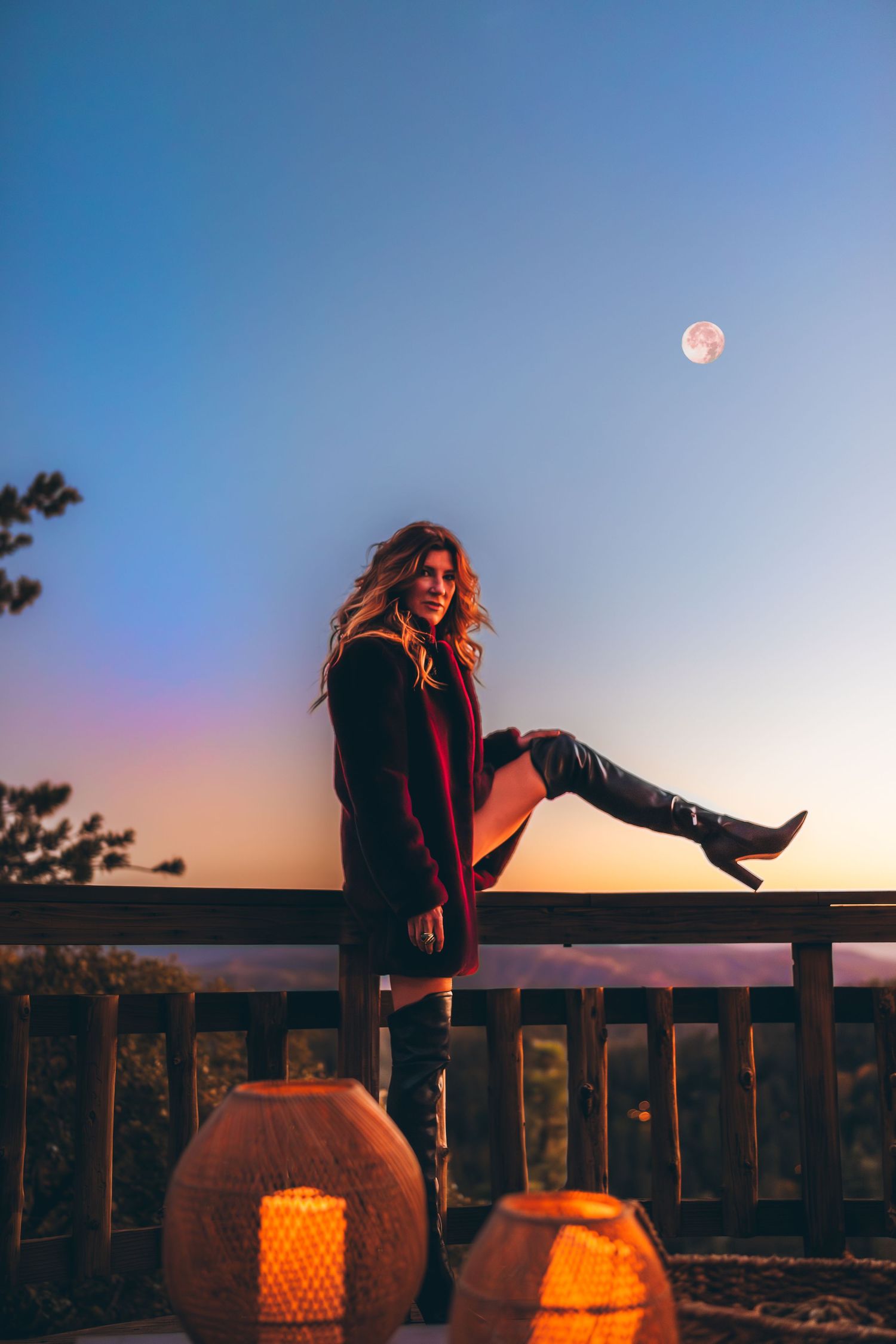 Silhouette on deck with glowing pumpkins at dusk under full moon.