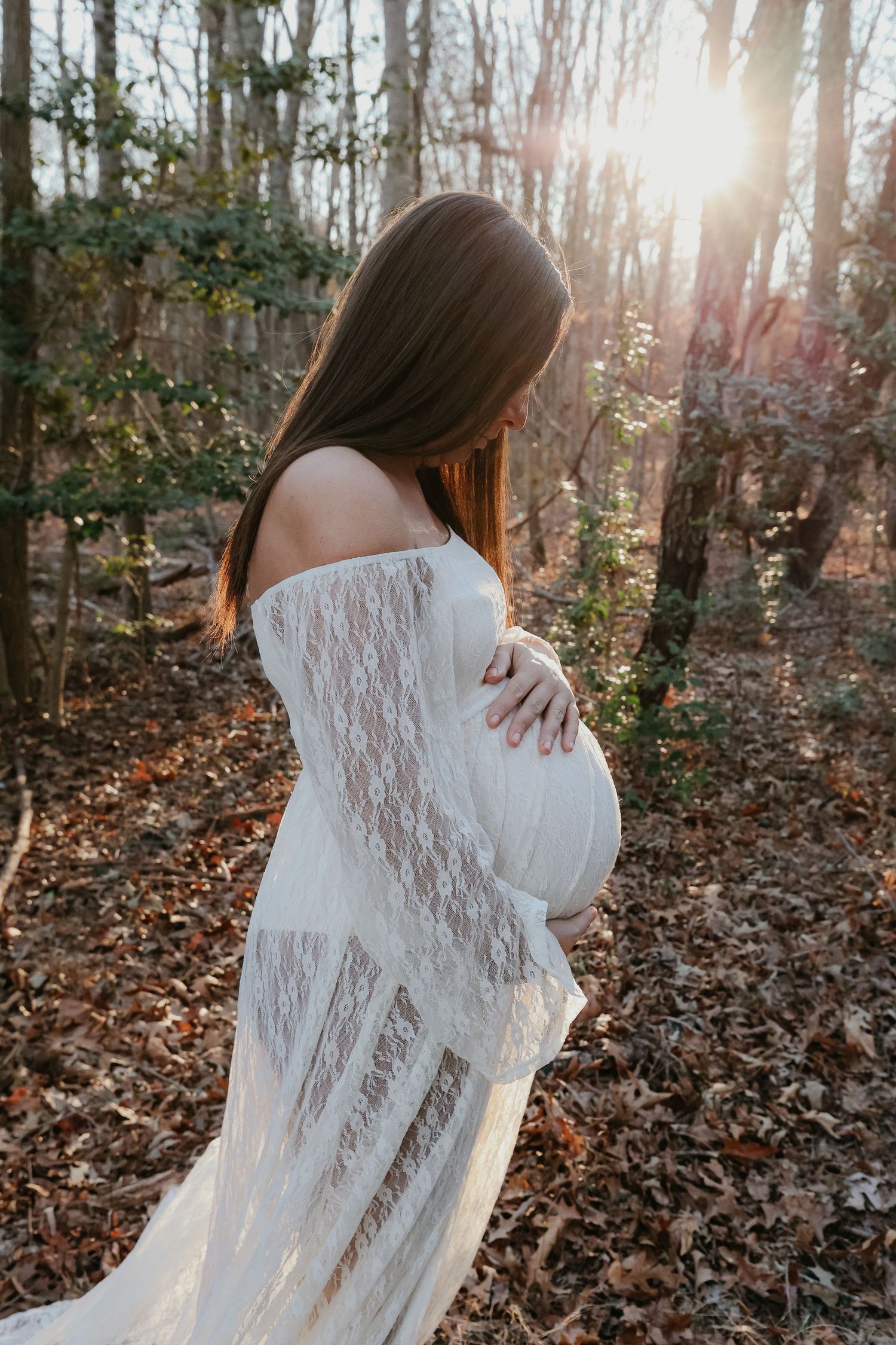 An ethereal maternity photo captures a side profile silhouette against sunlit woods.