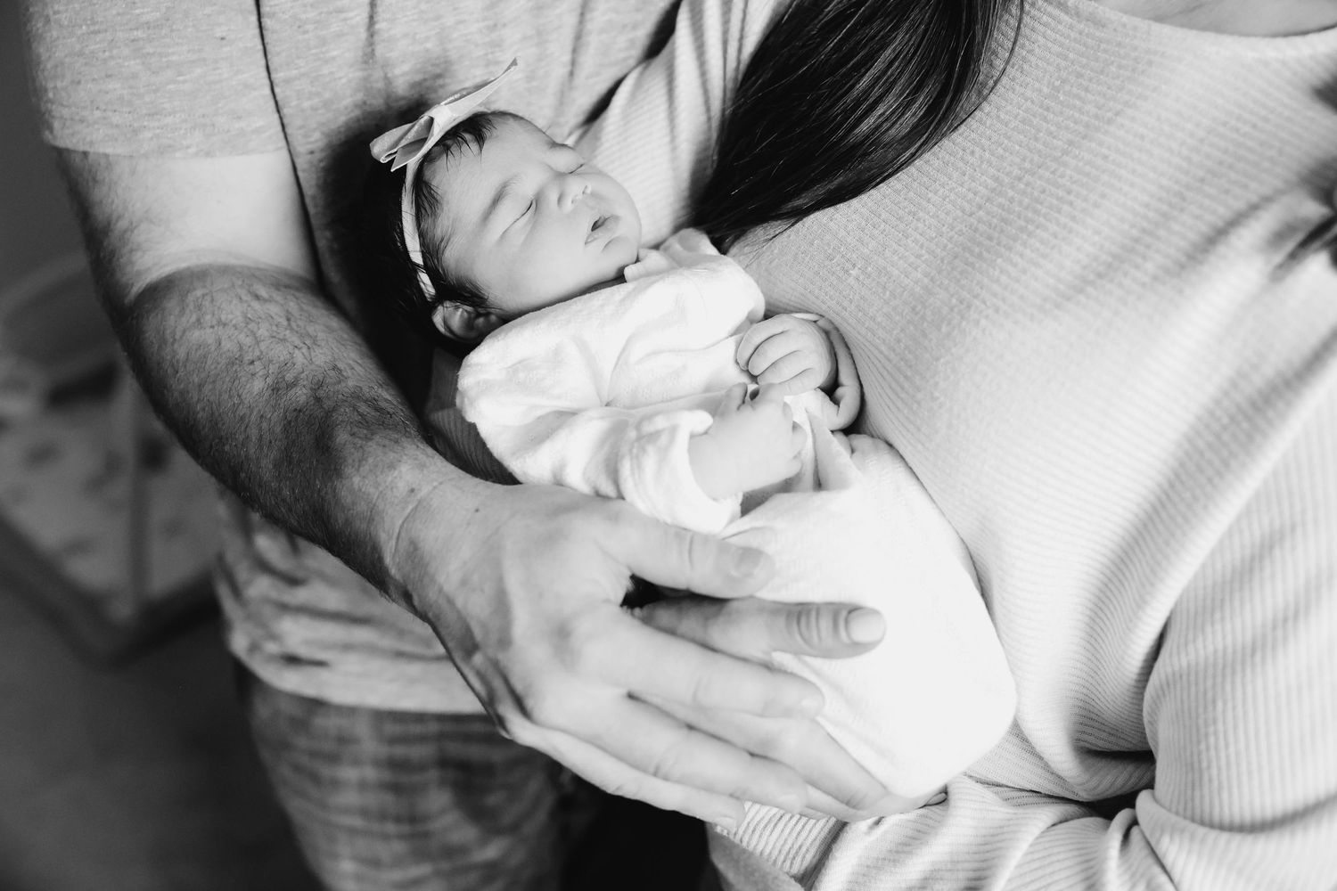 Black and white photo of tender hands cradling a sleeping newborn wrapped in white.