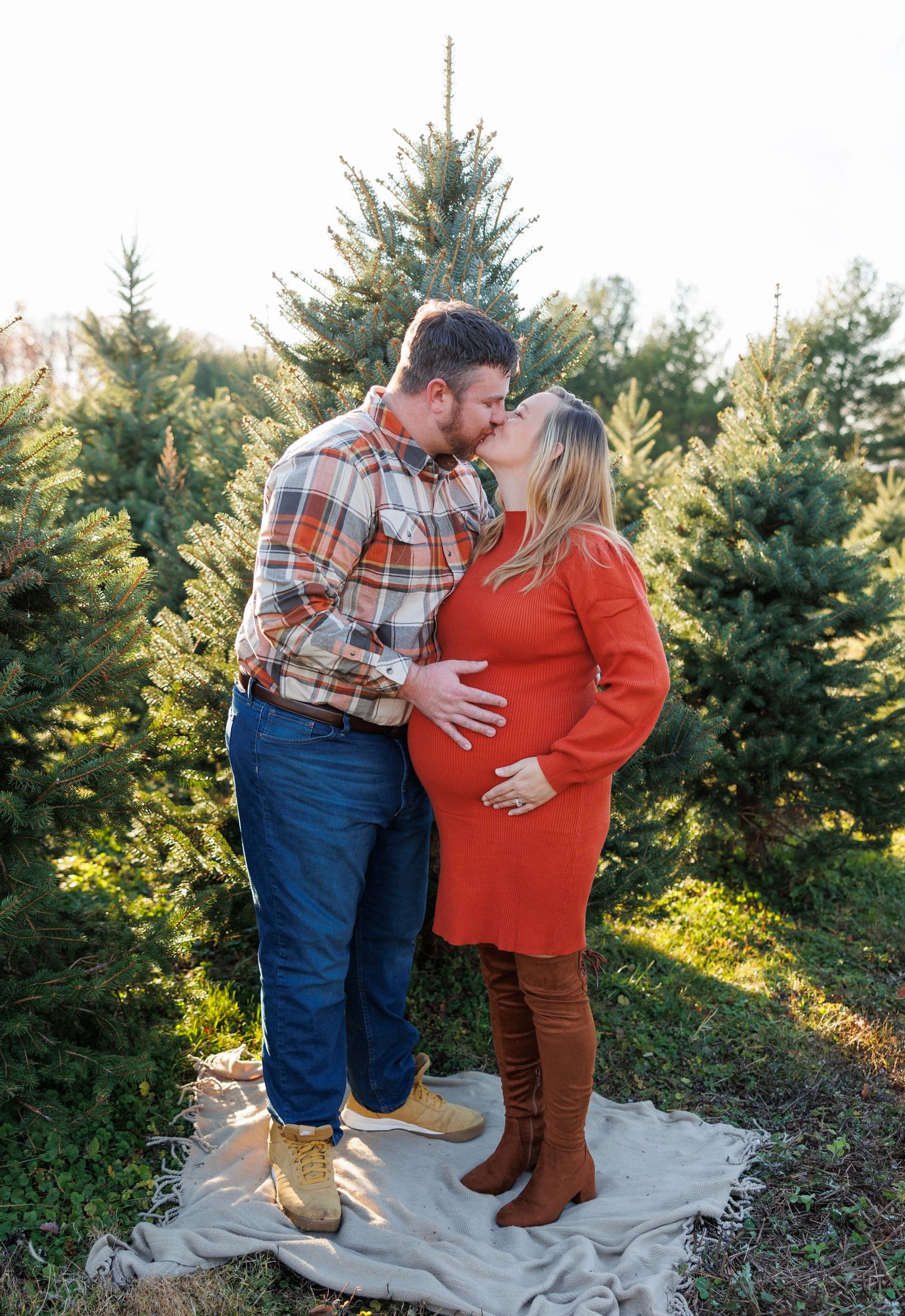 A couple shares a tender moment on a blanket surrounded by evergreen trees at sunset.