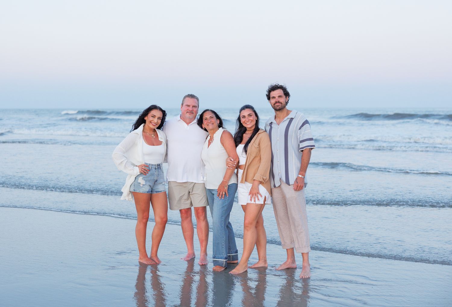 Group of people enjoying a sunset beach walk together while wearing light casual summer attire.