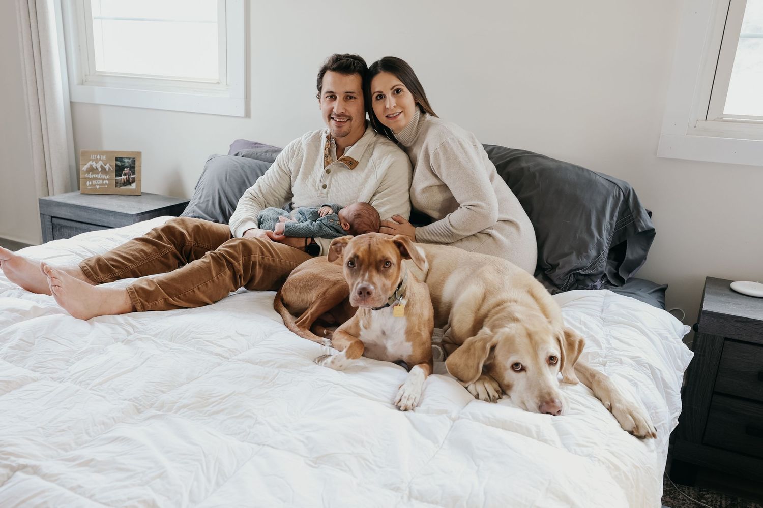 Couple relaxing on bed with two golden retriever dogs in cozy bedroom setting.