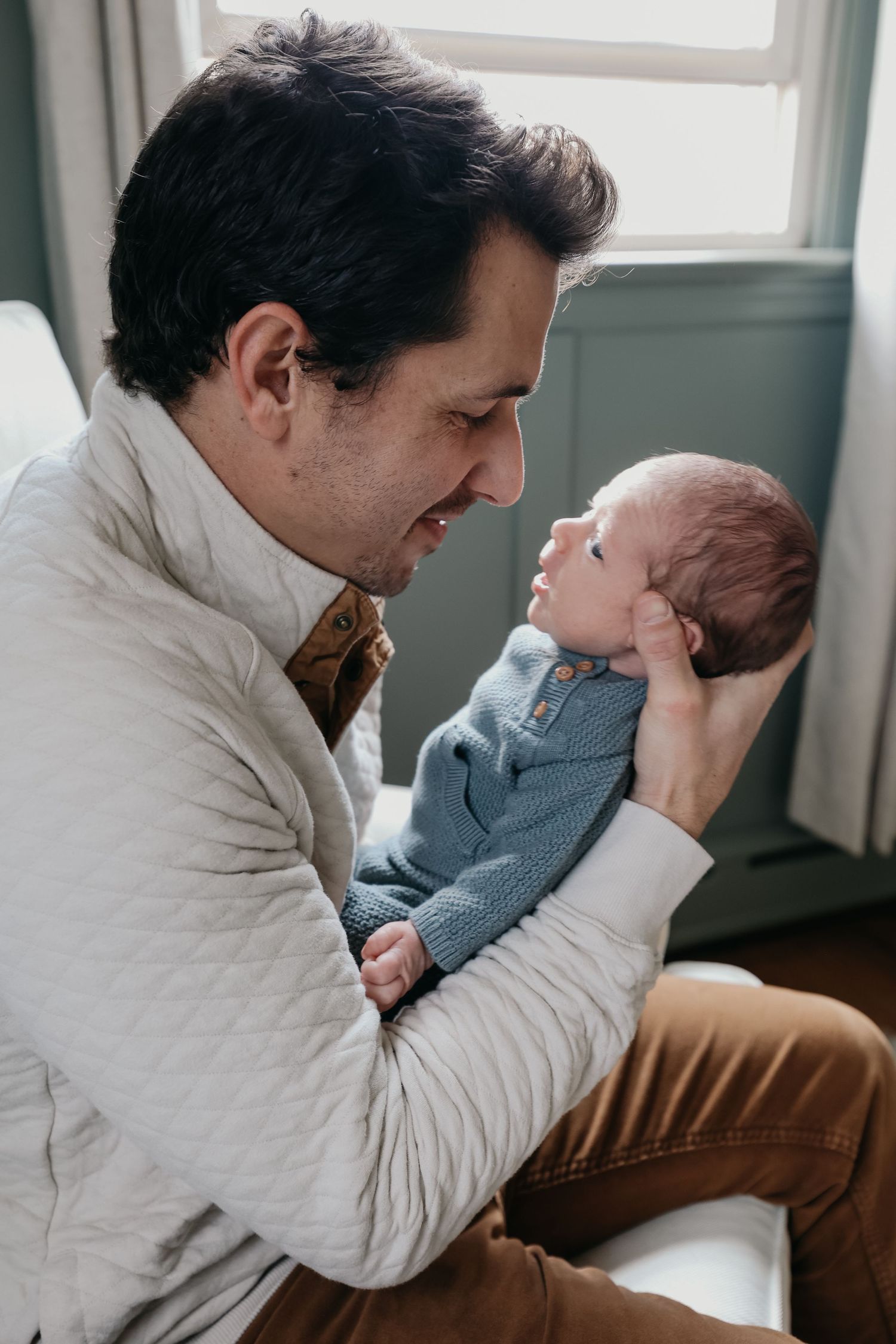 A tender moment between parent and newborn baby by a window in natural light.