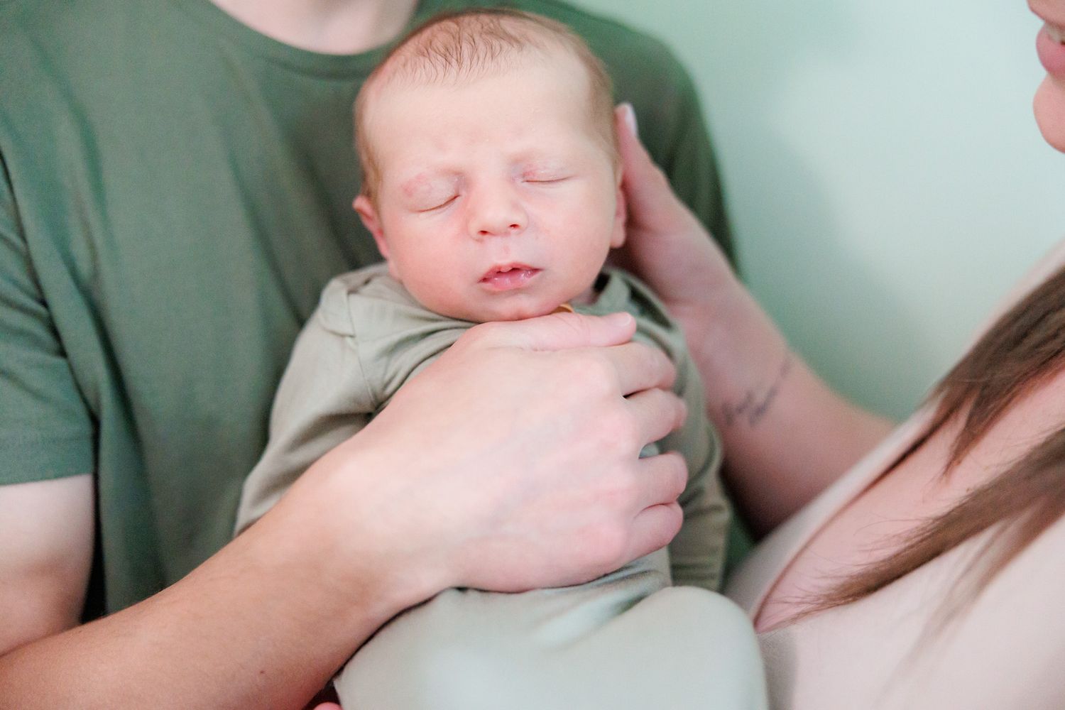 A sleeping infant swaddled in mint green bedding rests peacefully while being gently cradled.