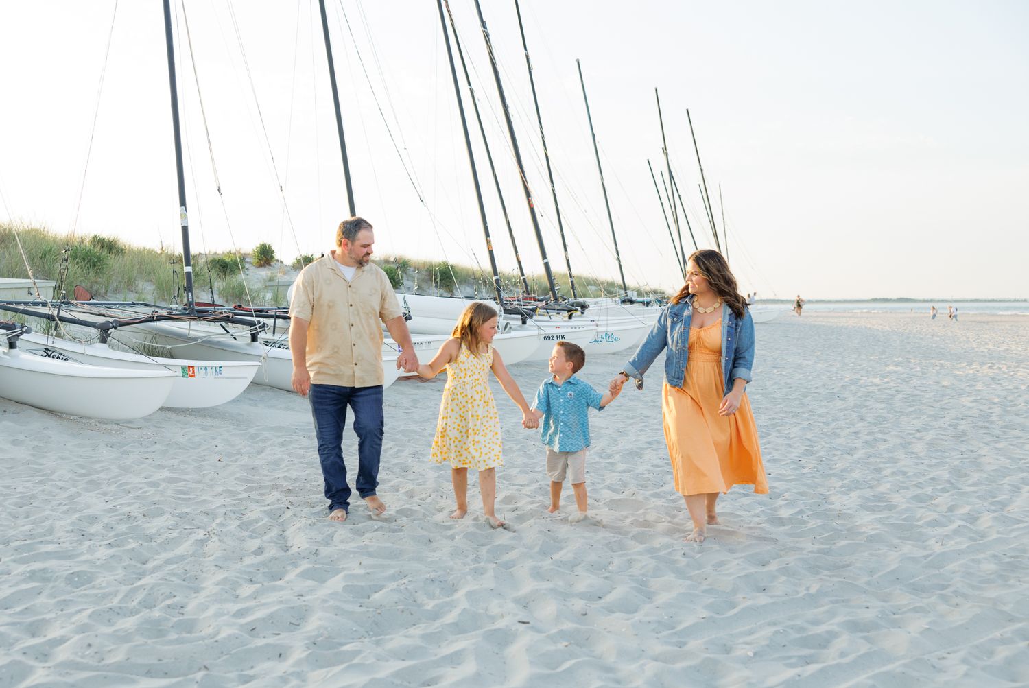 People wearing colorful dresses walk along a sunny white sand beach with ocean views in the background.