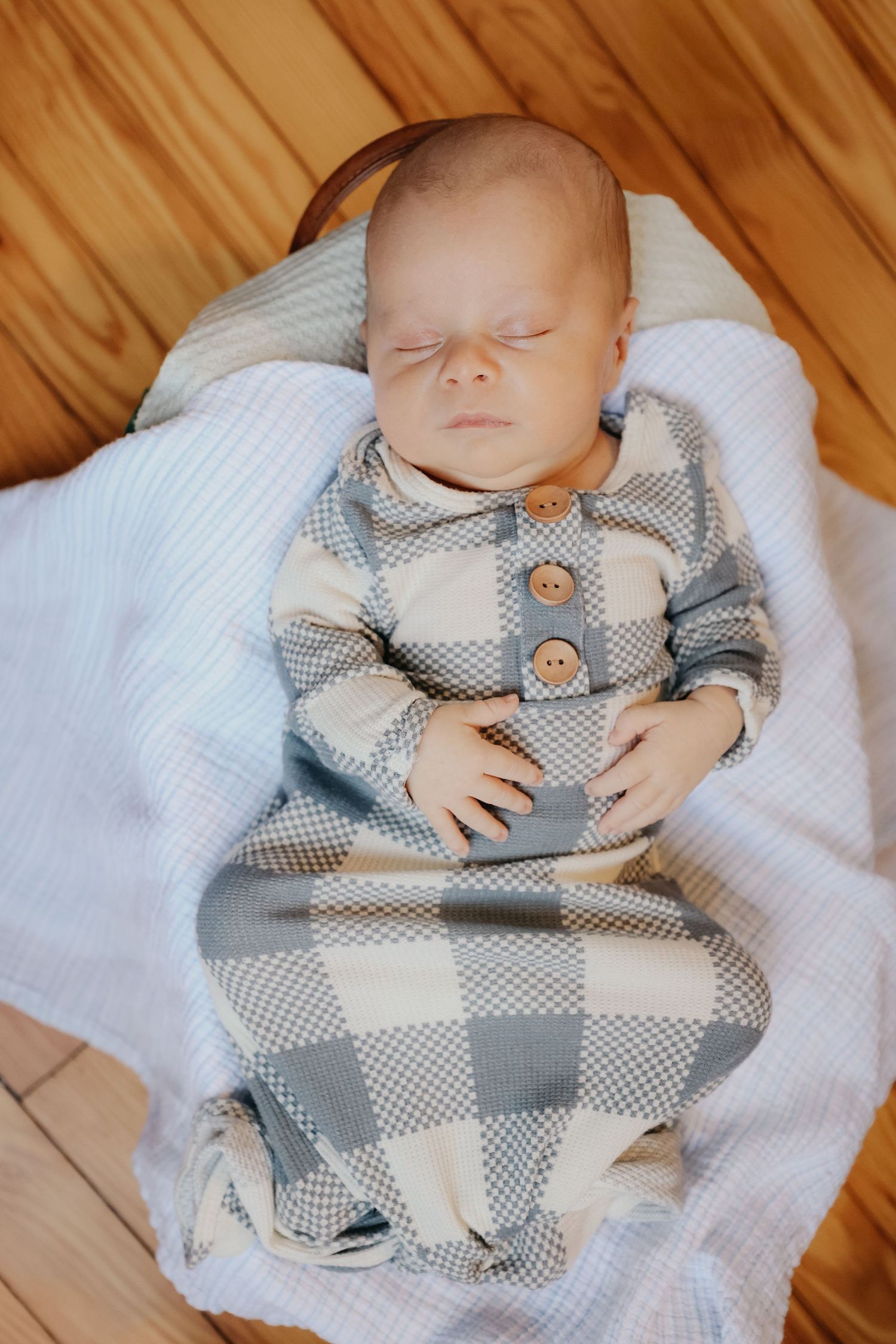 Sleeping baby wearing gray plaid outfit with bowtie on white blanket.