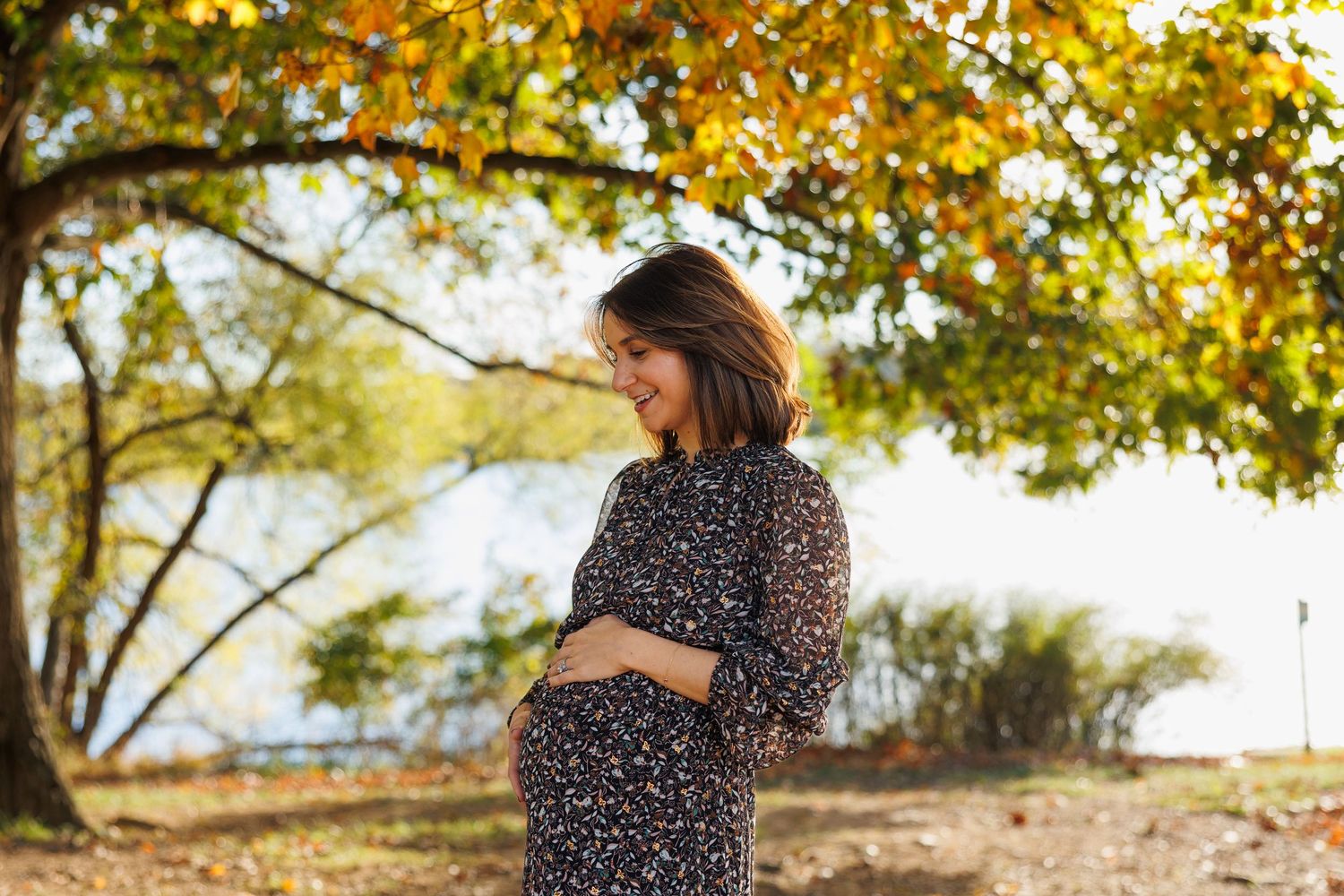 A person in a polka dot dress stands among autumn trees with golden leaves during a fall photoshoot.