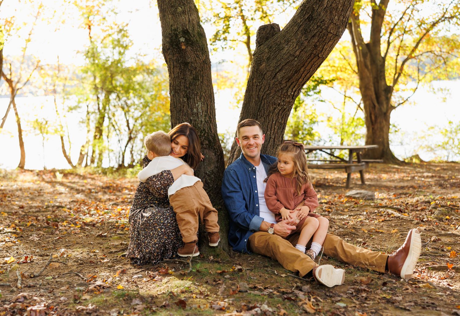 A group sits together under autumn trees during an outdoor gathering in a wooded area.