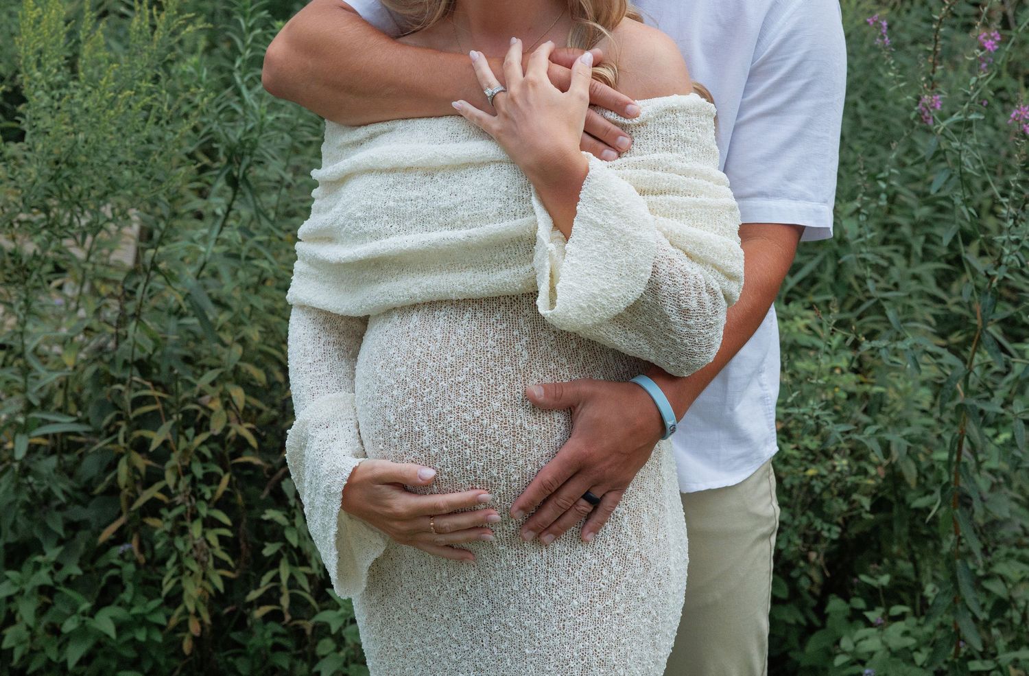 A series of maternity photos showing a couple embracing in a lush green garden setting, wearing white clothing.
