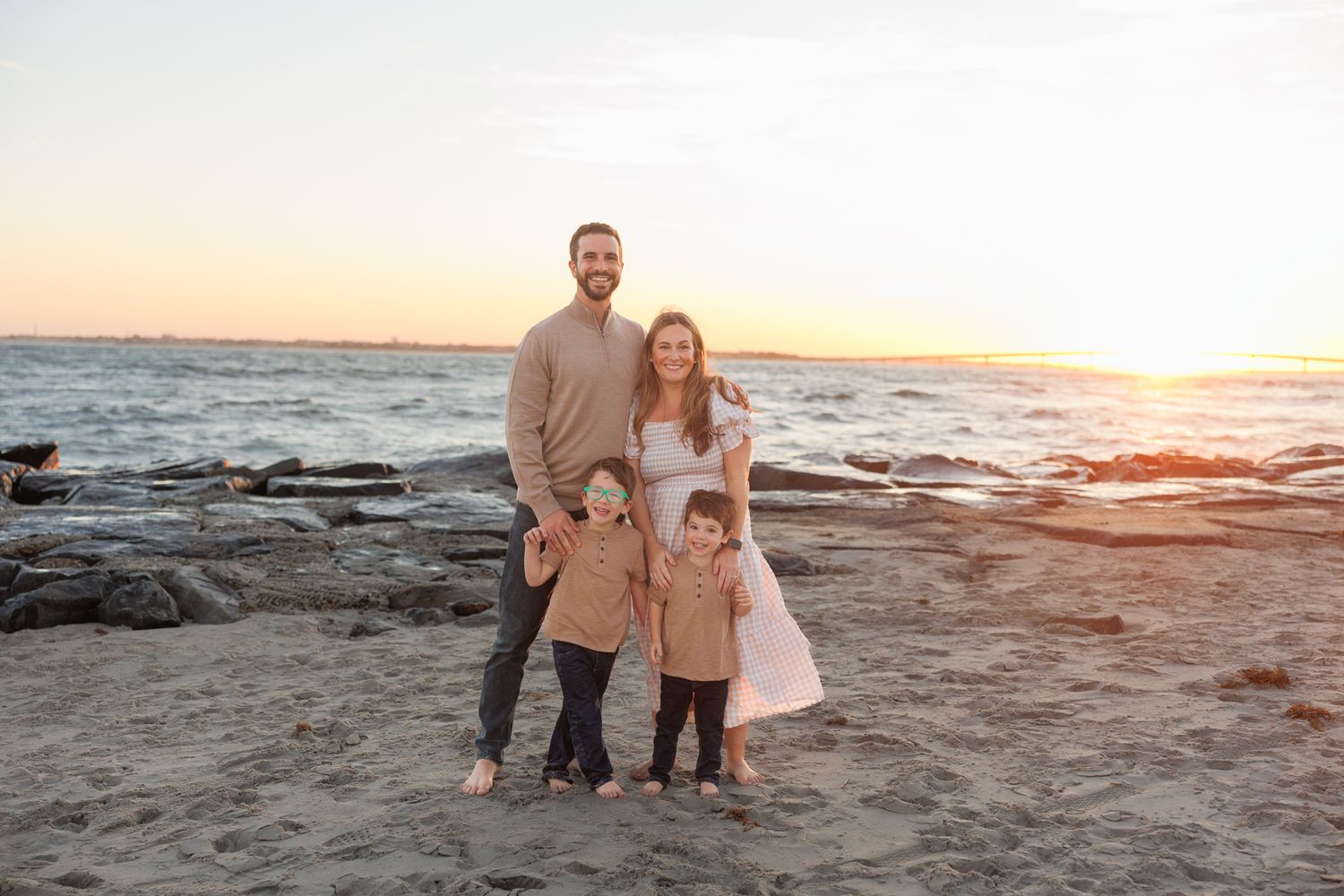 Family enjoys a sunset photoshoot on a sandy beach with ocean waves and golden light in the background.
