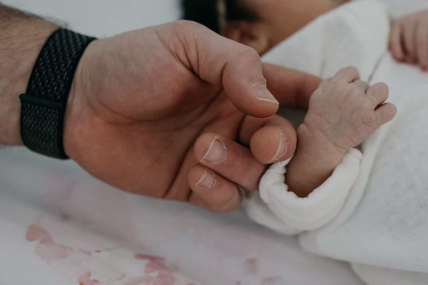Close-up of adult hand holding tiny newborn feet against patterned fabric.